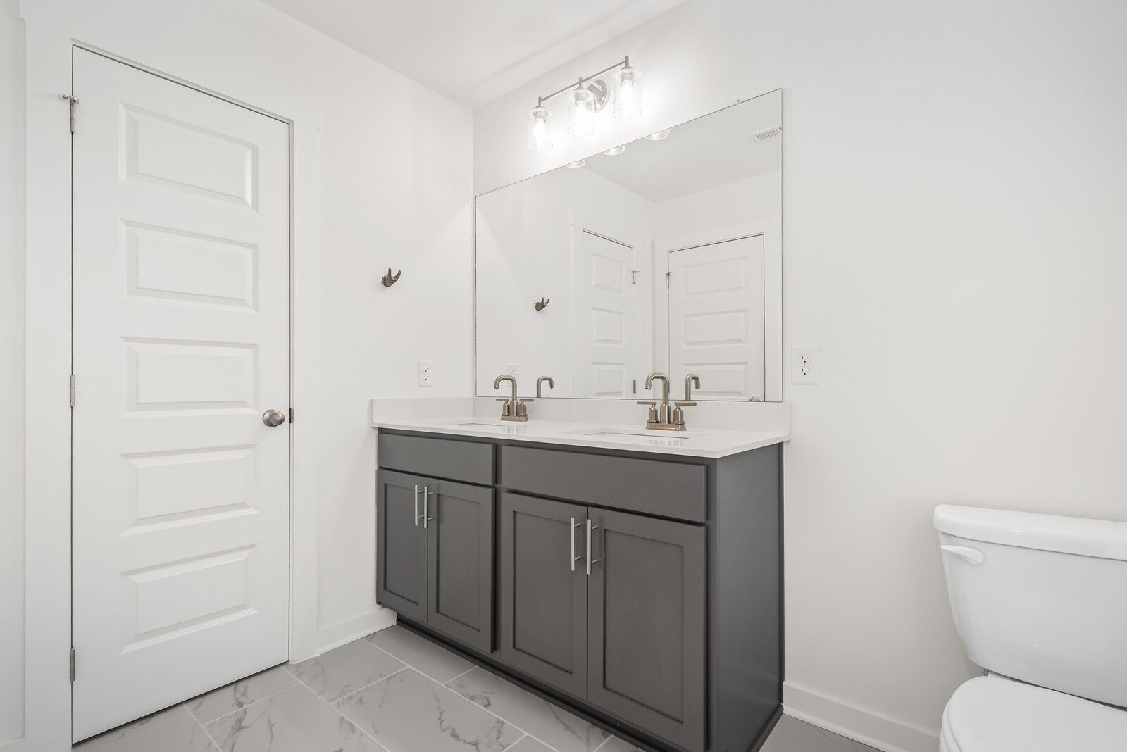 Modern master bathroom featuring double vanity with gray cabinets, large mirror, and white toilet in Davidson Homes The Gordon C, White House, TN