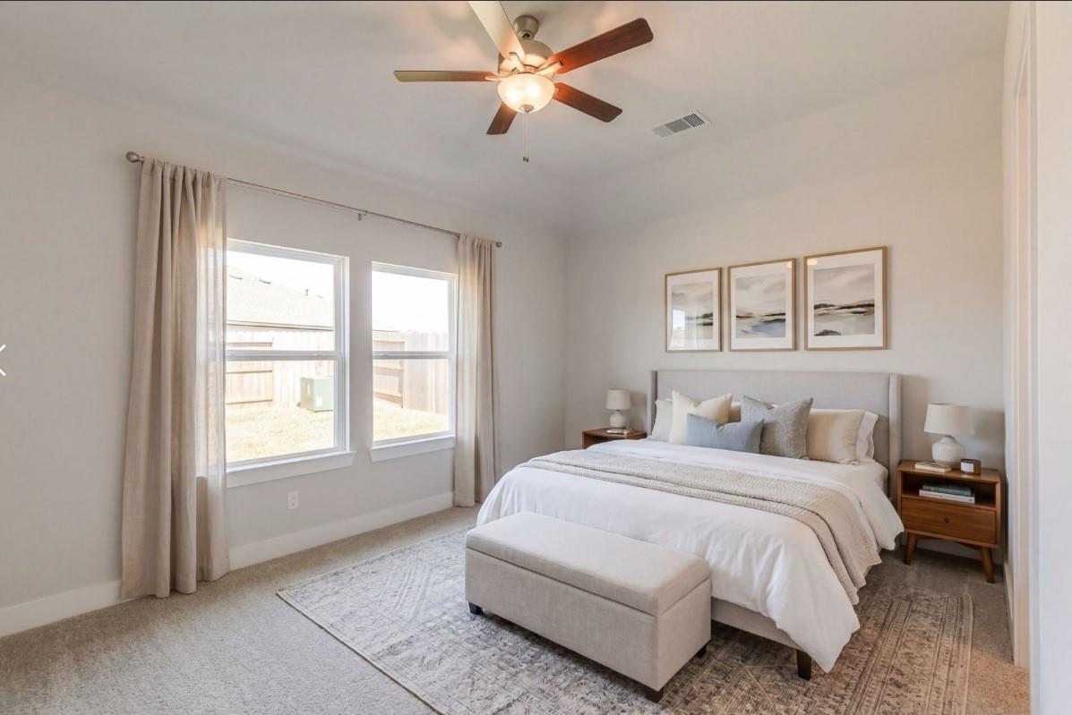 Serene bedroom with king bed, neutral bedding, ceiling fan, large windows, and seascape wall art in Davidson Homes The Luna J, Katy TX