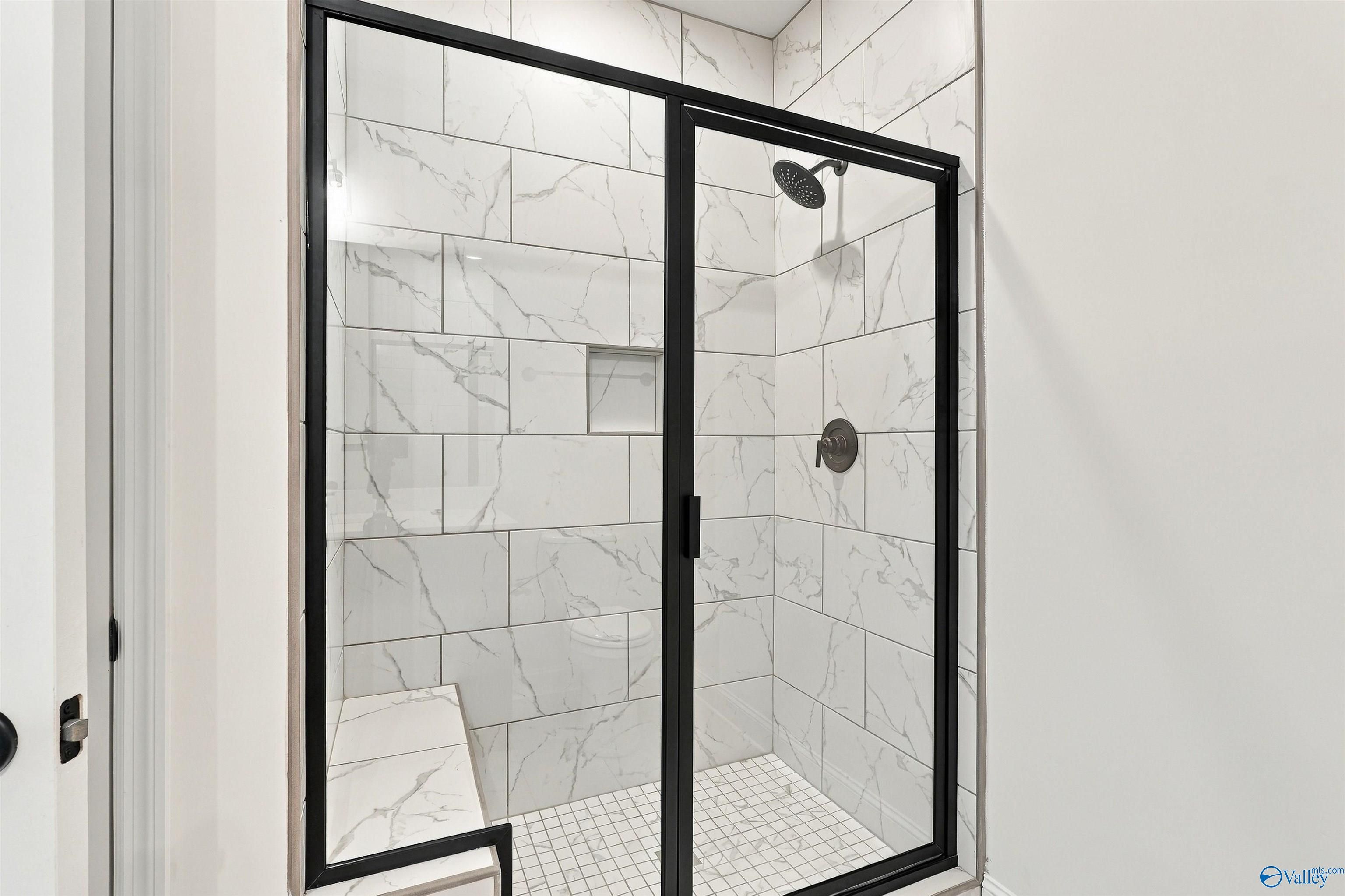 Marble-tiled walk-in shower with black frame, built-in bench, and niche in Davidson Homes Valencia bath, Huntsville, AL