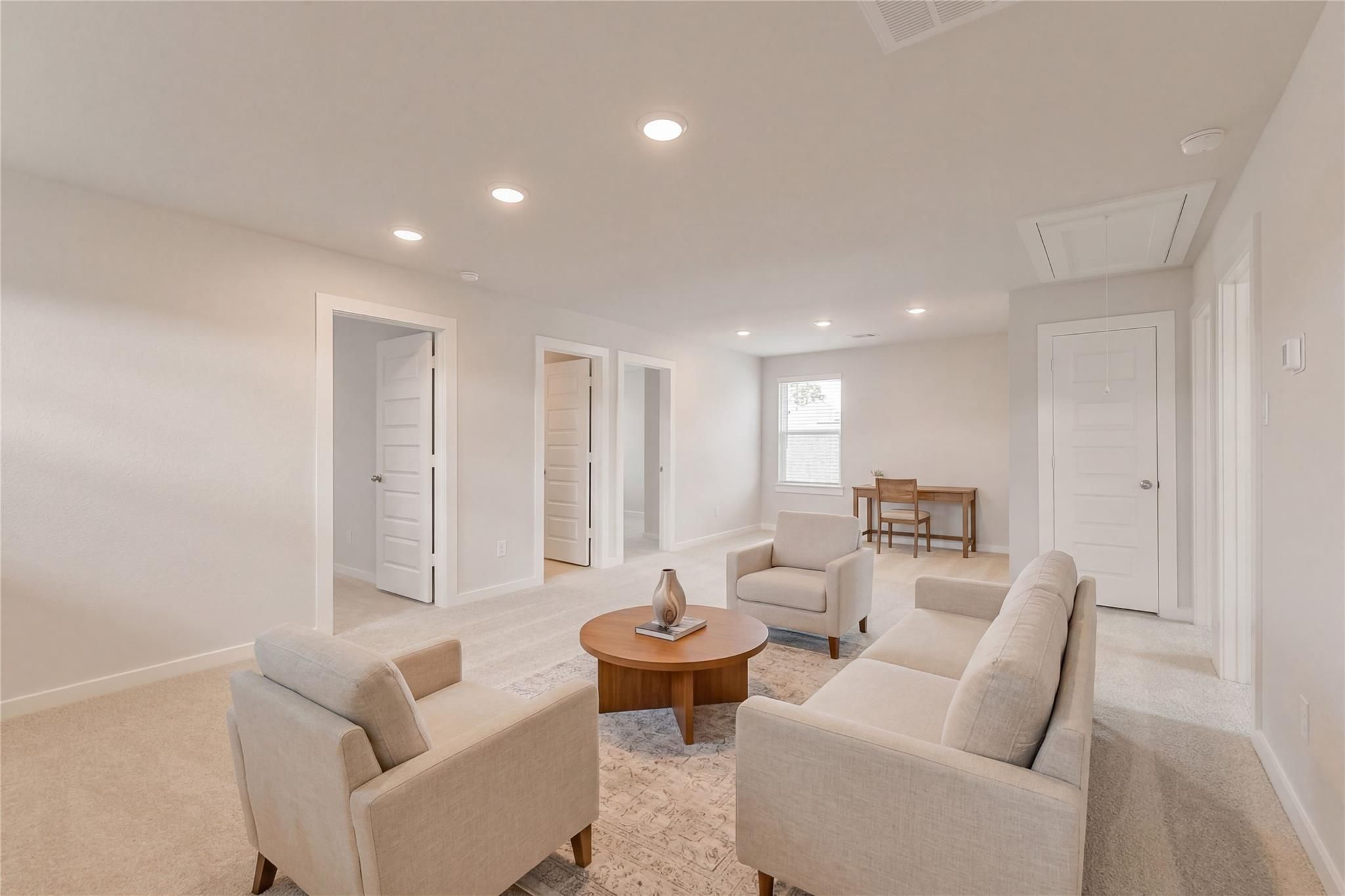 Cozy neutral-toned living room with beige sofa, armchairs, wooden coffee table, and desk in Davidson Homes The Brazos E, Cleveland Texas