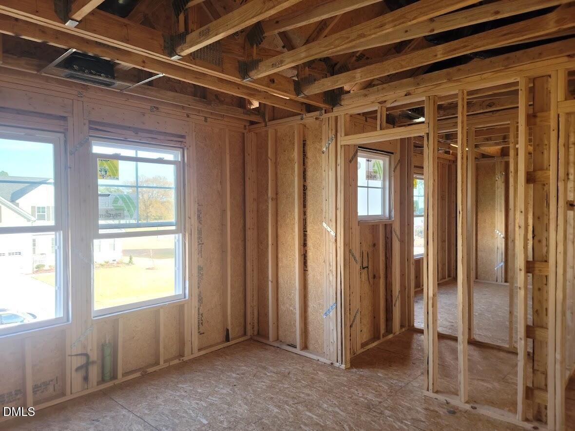 Framed bedroom interior with exposed wooden beams, insulation, and windows overlooking neighborhood in The Willow G 5-bedroom home, Angier, NC
