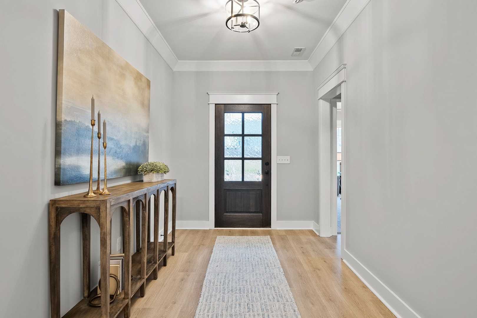 Spacious foyer in The Oxford home design featuring console table, abstract seascape art, dark wood door, hardwood floors, and chandelier