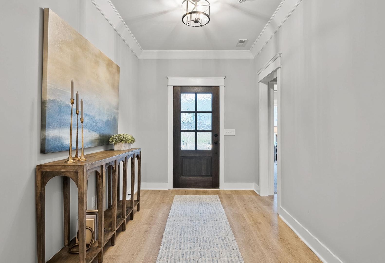 Spacious foyer in The Oxford home design featuring console table, abstract seascape art, dark wood door, hardwood floors, and chandelier