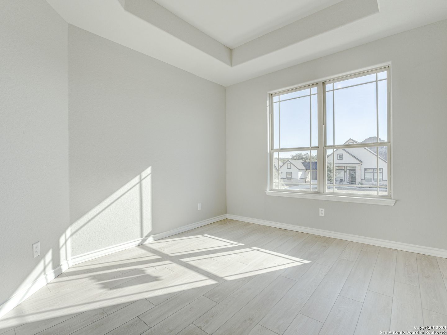 Sunlit secondary bedroom with tray ceiling, large windows, gray walls, wood floors in Davidson Homes Summerlin A, Castroville Texas