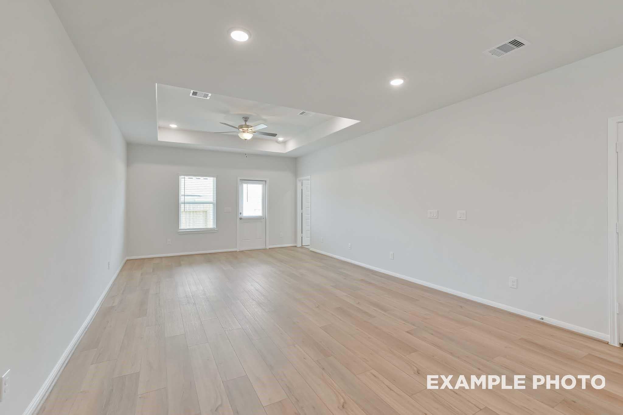 Spacious living room with tray ceiling, ceiling fan, large windows, and light wood floors in Davidson Homes The Frio F, Conroe, Texas