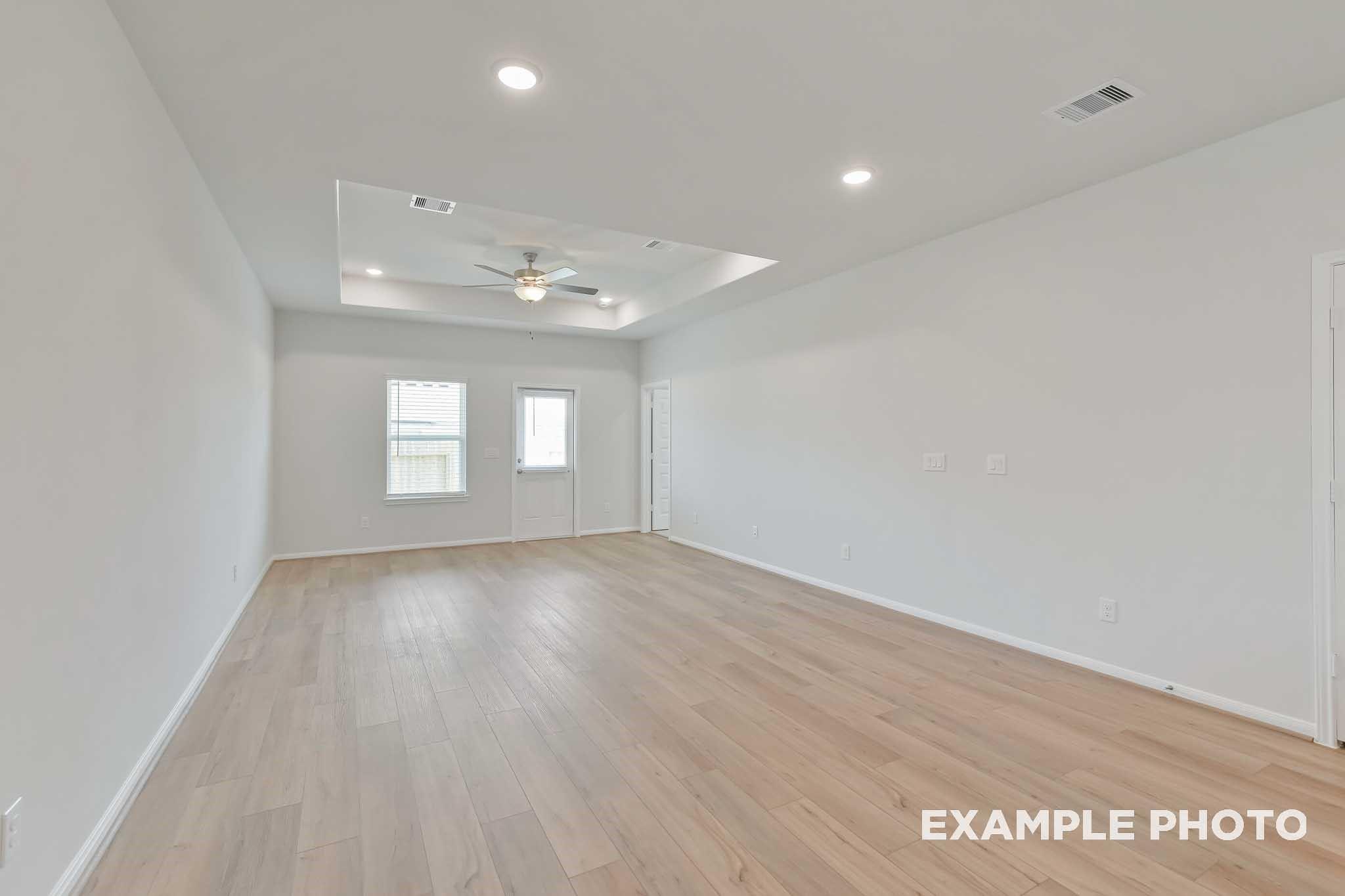 Spacious living room with tray ceiling, ceiling fan, large windows, and light wood floors in Davidson Homes The Frio F, Conroe, Texas