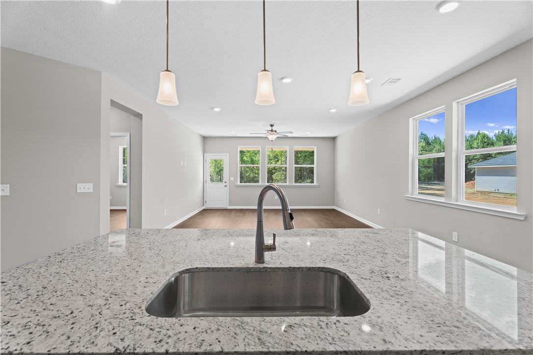 Modern kitchen with granite counters, stainless sink, pendant lights, and open living area in Evermore Homes The Orion, Cusseta, Alabama