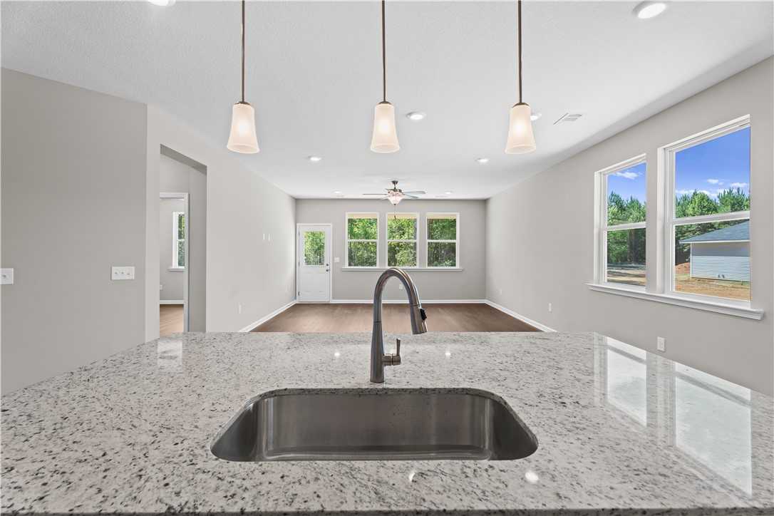 Modern open-concept kitchen with granite island, stainless sink, pendant lights in Evermore Homes The Orion, Cusseta, Alabama