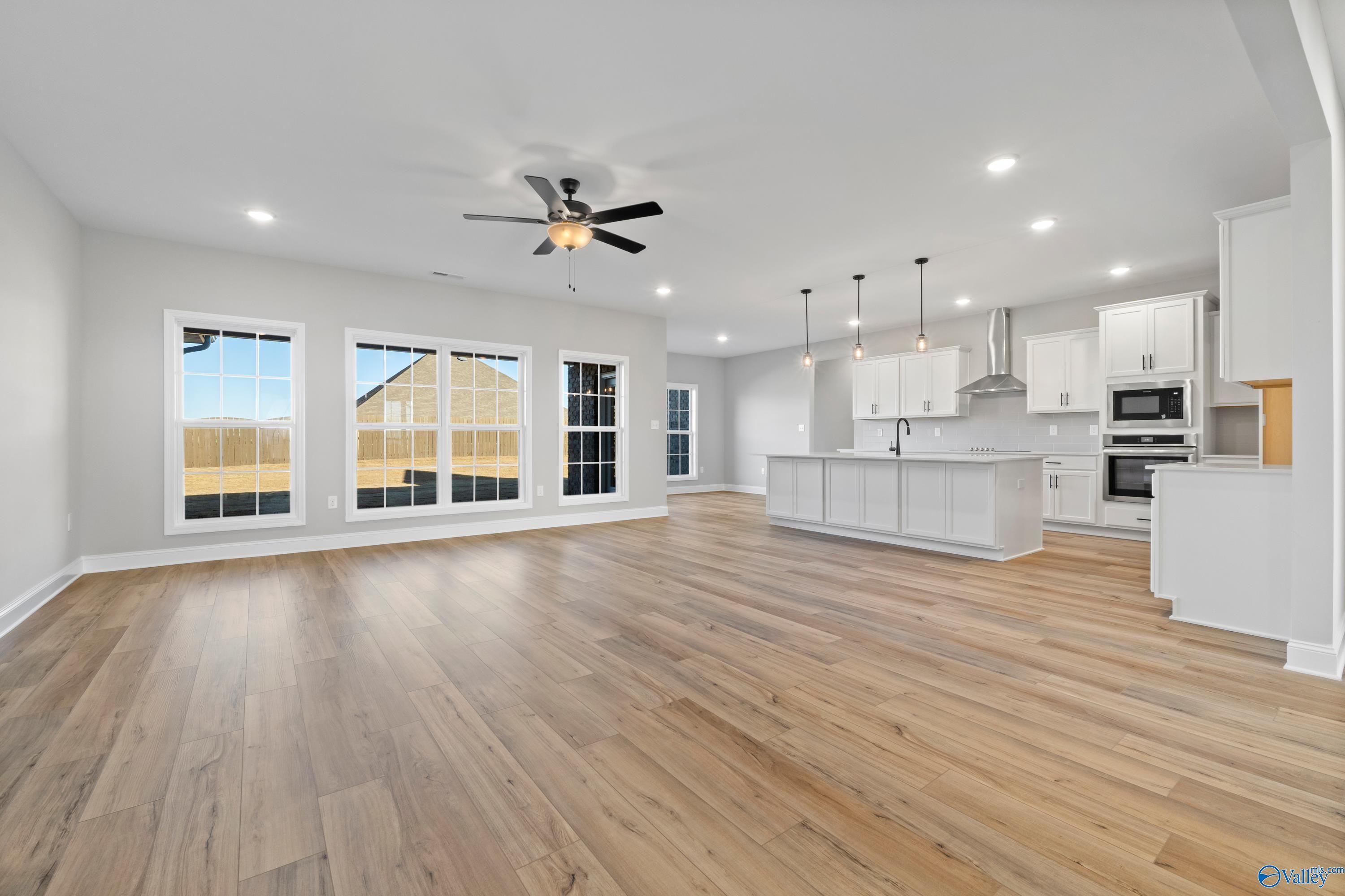 Open-concept kitchen and living area with white cabinets, hardwood floors, large windows, and ceiling fan in Davidson Homes The Valencia, Meridianville, Alabama