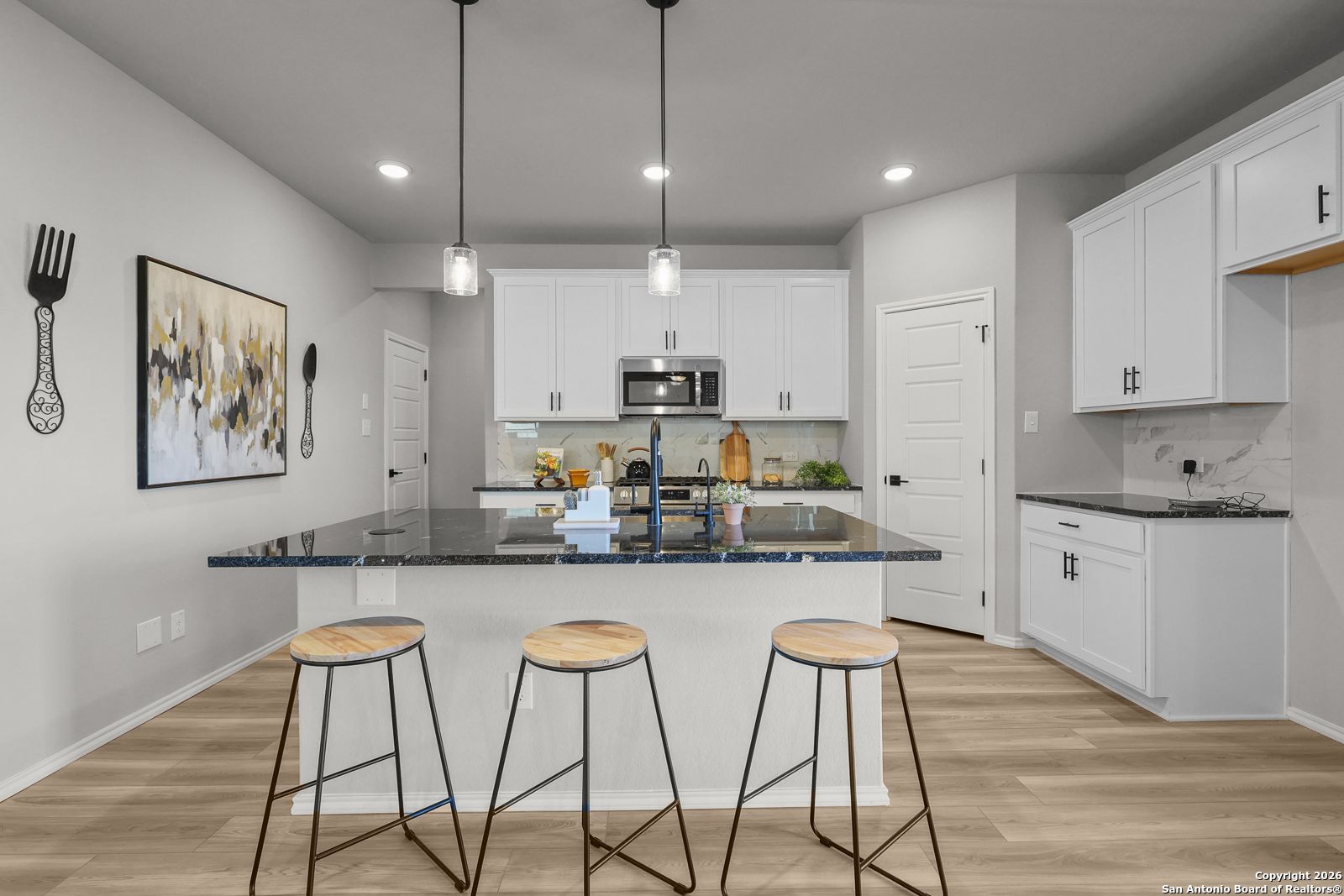 Modern kitchen featuring white shaker cabinets, black granite island, stainless appliances, and bar stools in Davidson Homes The Murray K, San Antonio