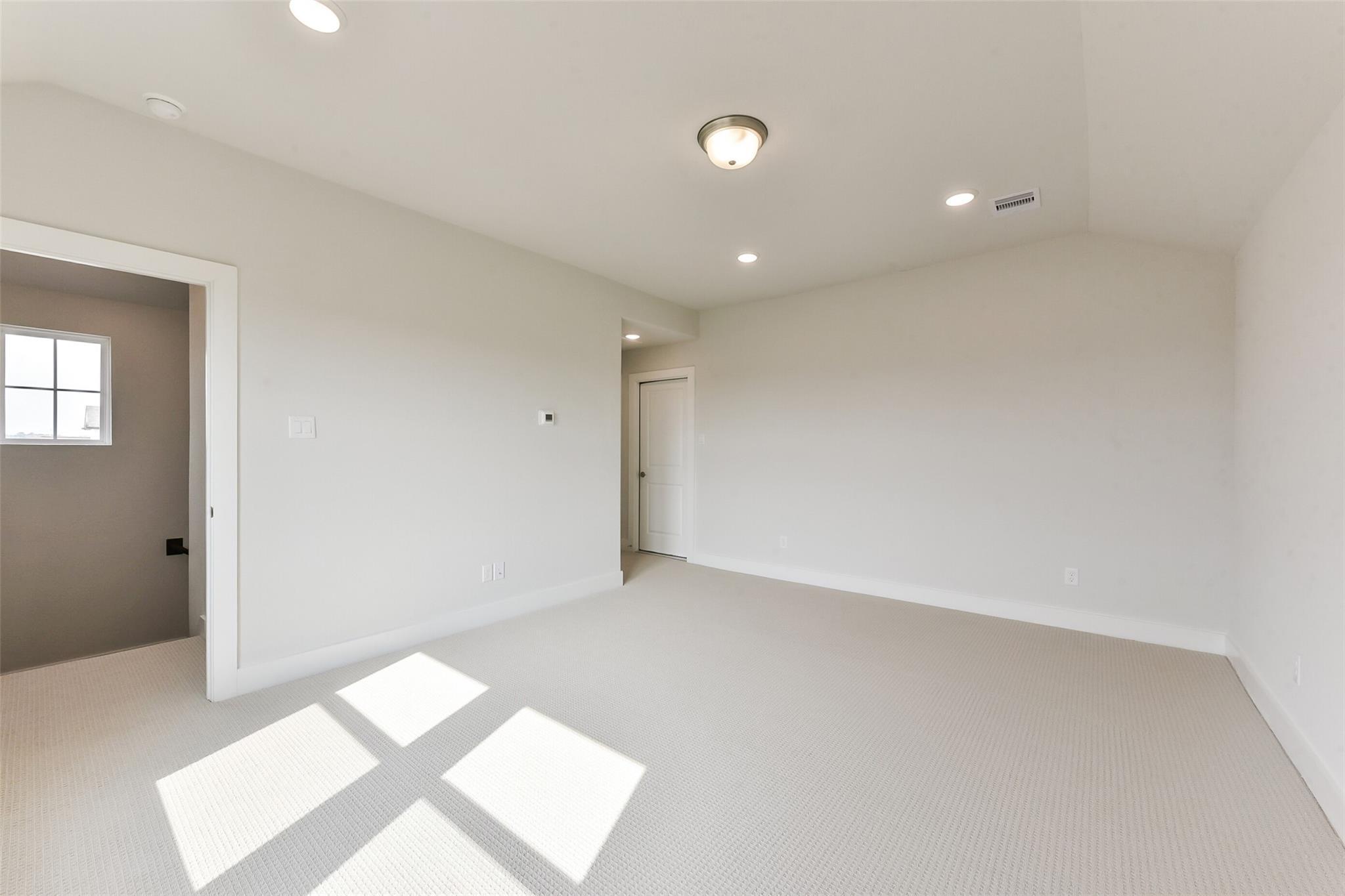 Empty bedroom with beige walls, carpeted floors, recessed lighting, and sunny windows in Davidson Homes The Edward A, Lago Mar, Texas City