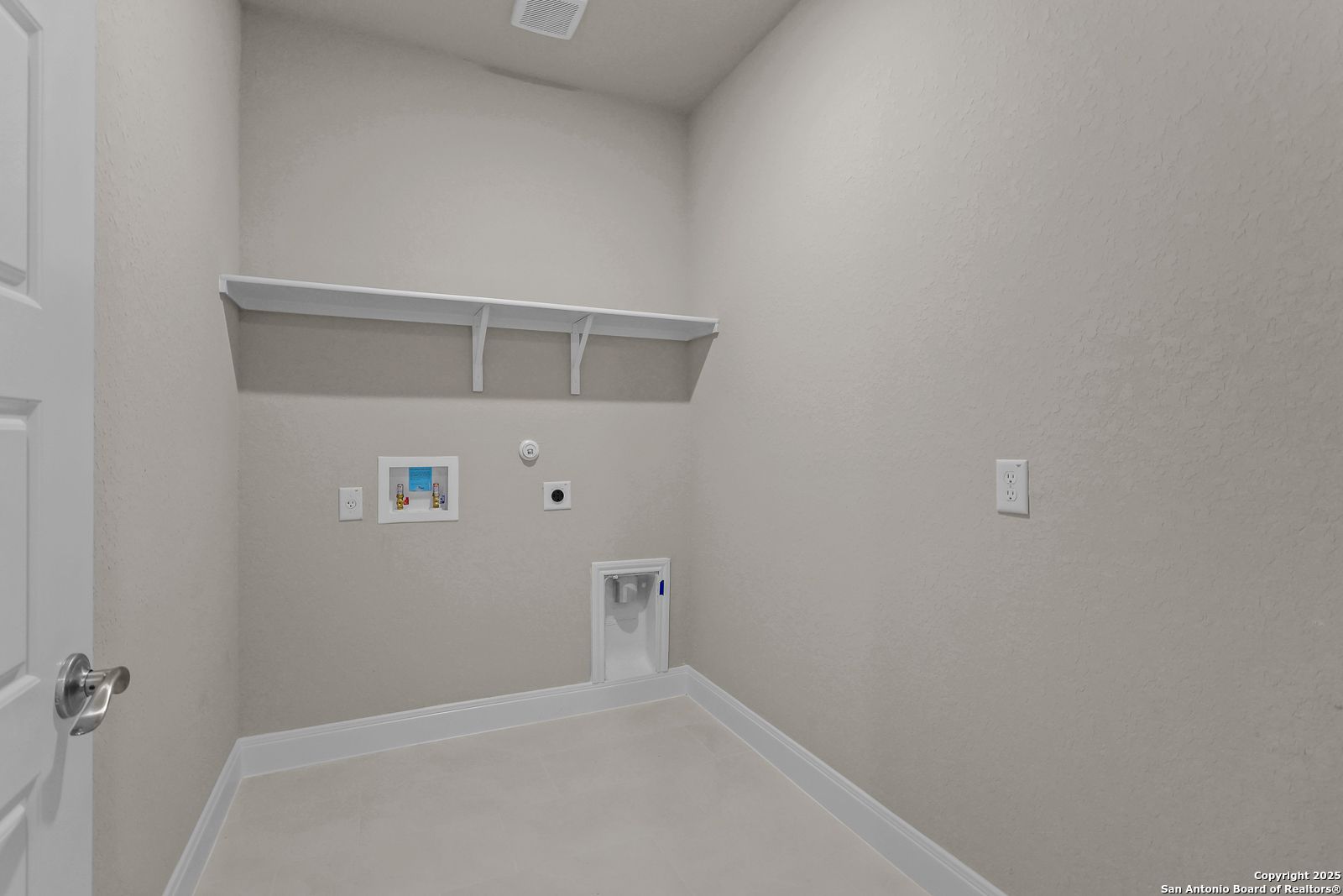 Spacious laundry room with white built-in shelves, washer-dryer hookups, beige walls in The Jennings G home, Castroville, Texas