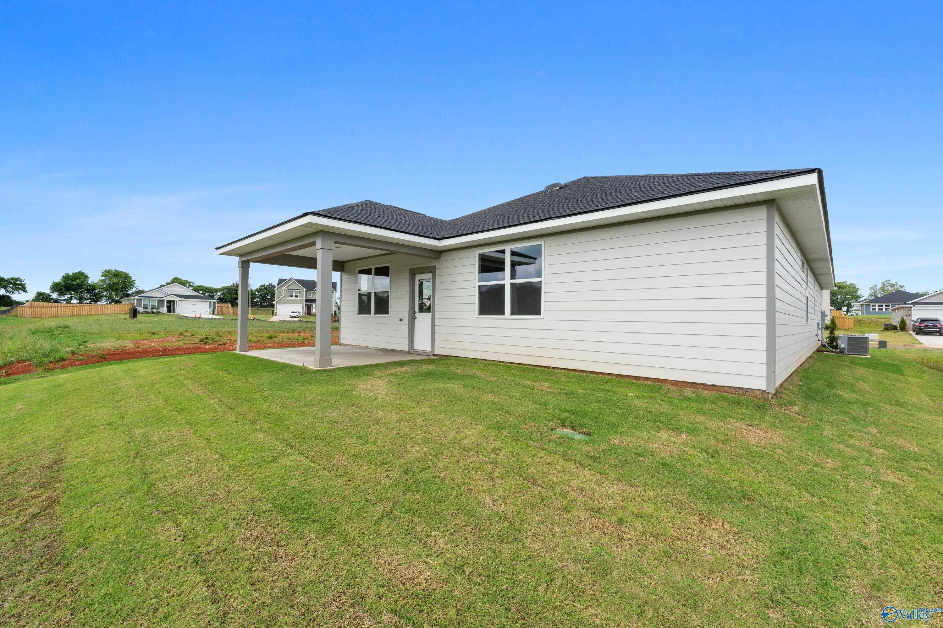 Back view of The Aurora 4-bedroom home by Evermore Homes with covered patio, white siding, and lush lawn in Carroll Green, Harvest, Alabama