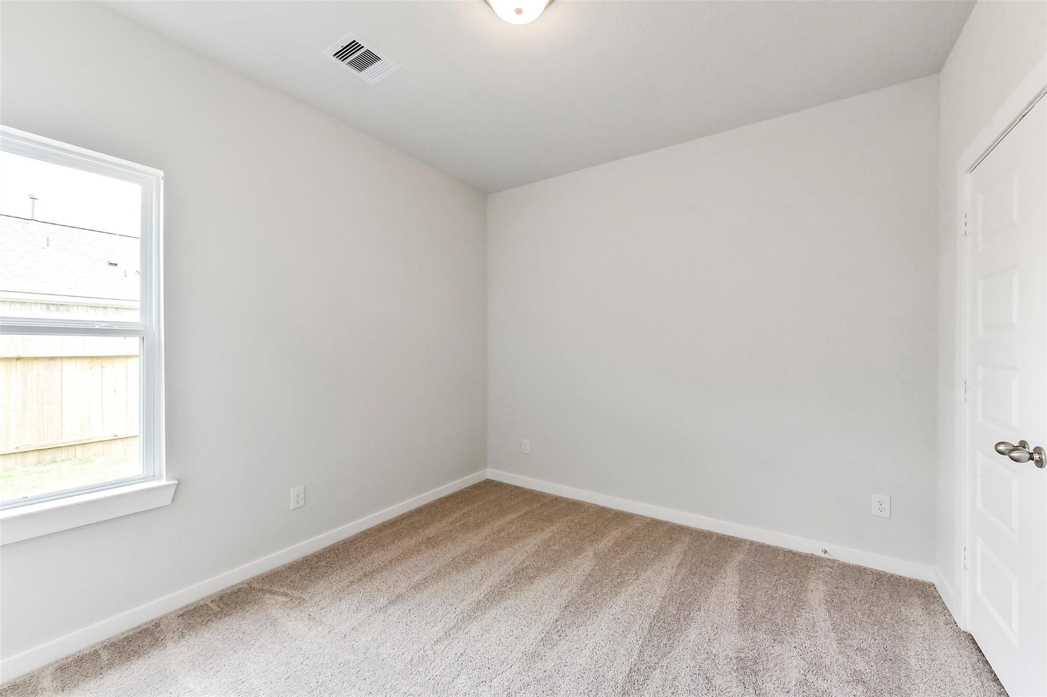Bright secondary bedroom with white walls, beige carpet, large window, and closet door in Davidson Homes The Costa B, Dayton, Texas
