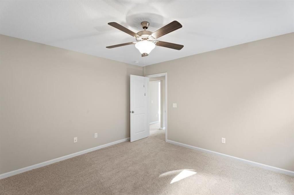 Spacious beige bedroom with ceiling fan, carpet, and open door in Davidson Homes The Washington, Phenix City, Alabama