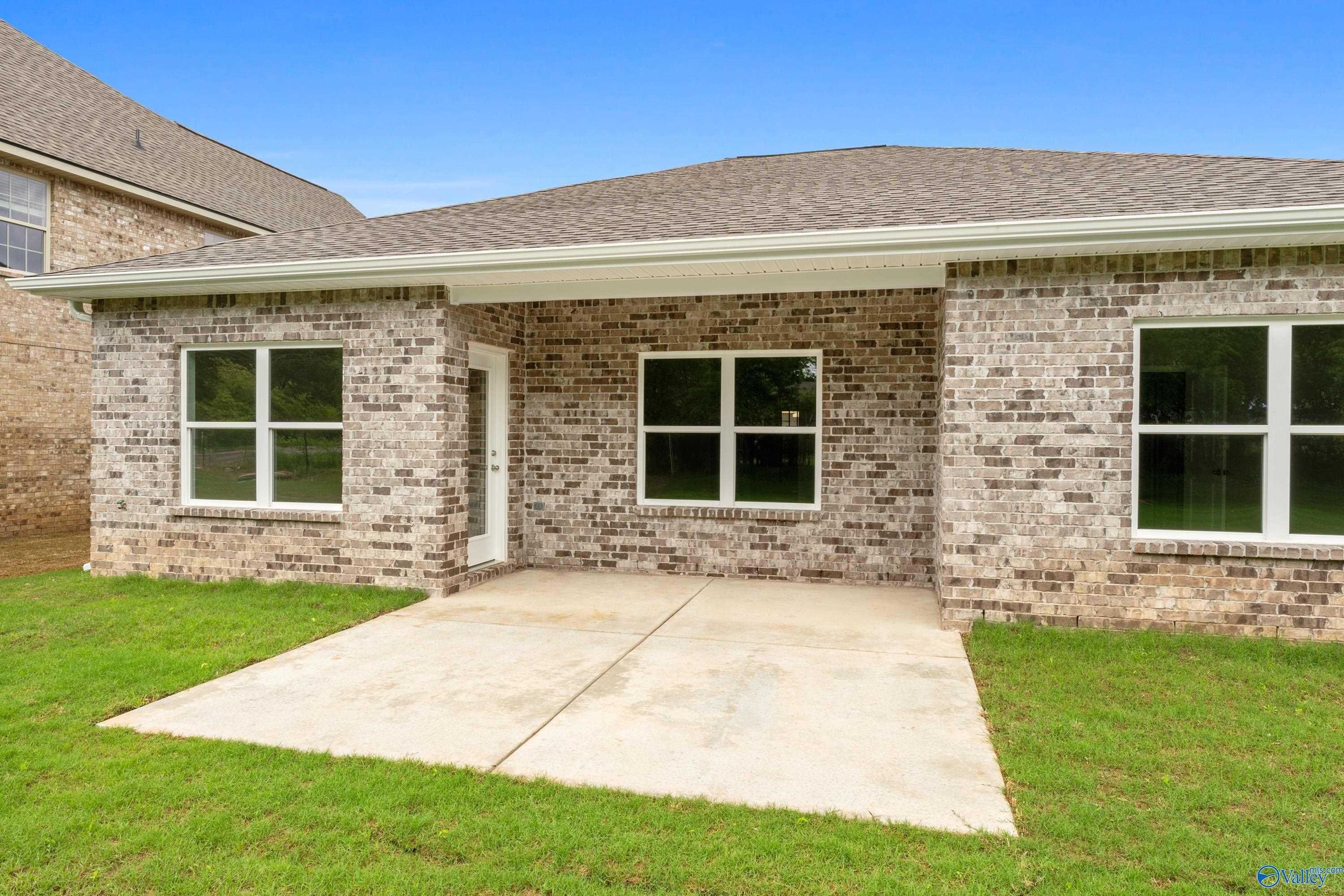 Single-story brick home exterior with covered porch, large windows, and lush green lawn in Jaguar Hills, Huntsville, Alabama - The Asheville C by Davidson Homes