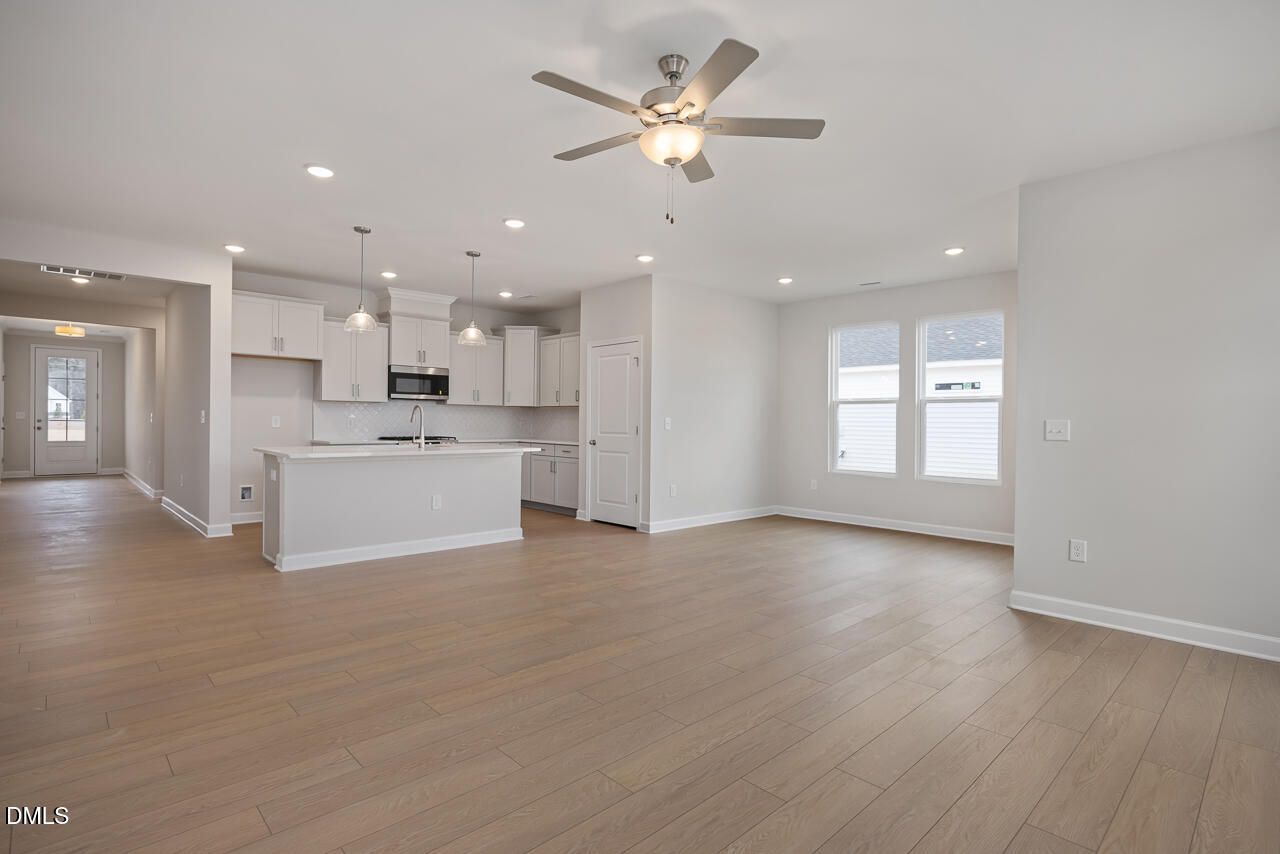 Spacious open kitchen with white cabinets, center island sink, and recessed lighting in modern living area with hardwood floors, The Daphne C by Davidson Homes, Lillington NC