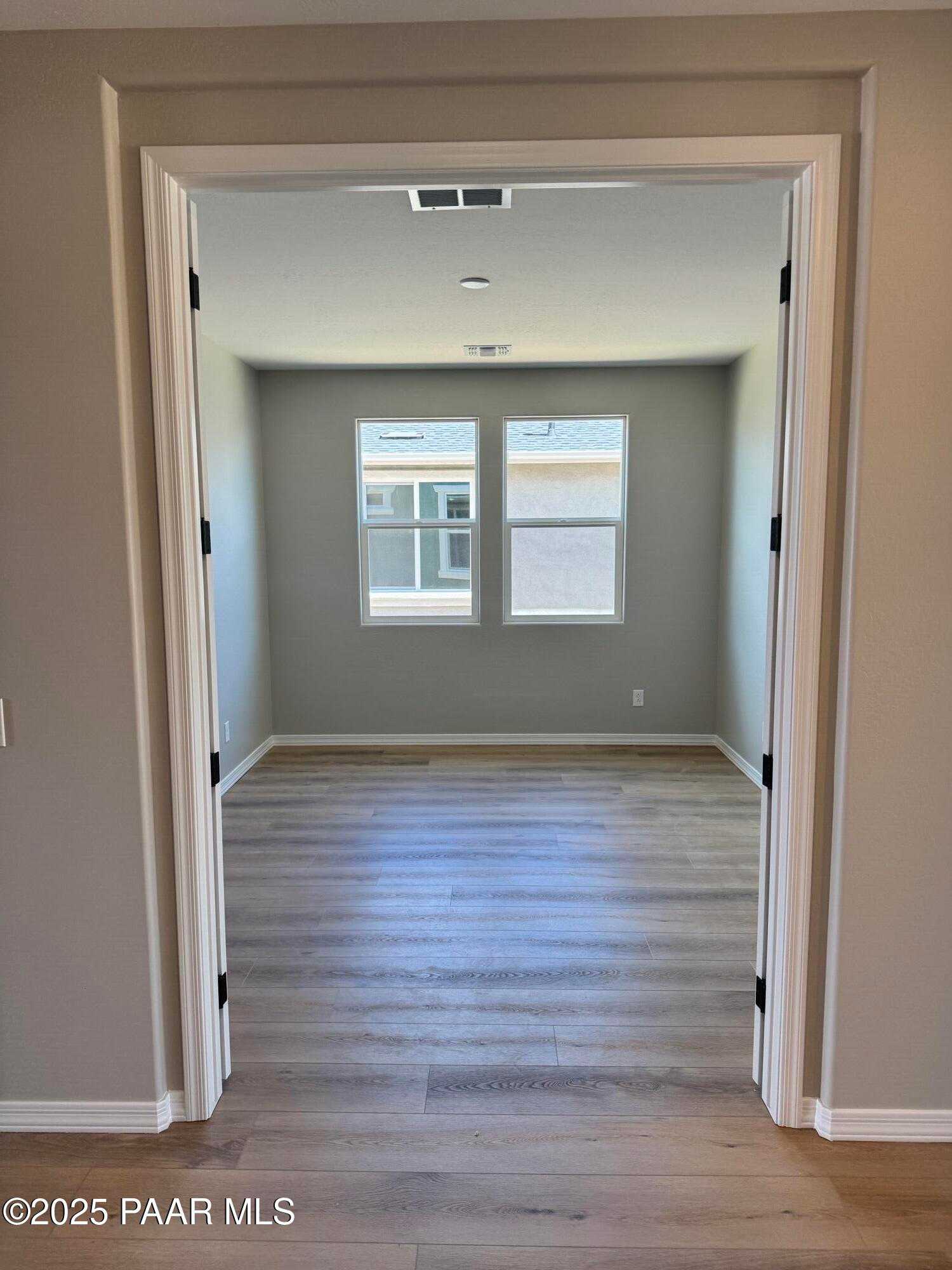 Spacious empty bedroom with dual windows, gray walls, and light hardwood floors in Davidson Homes Sheridan II B, Prescott AZ