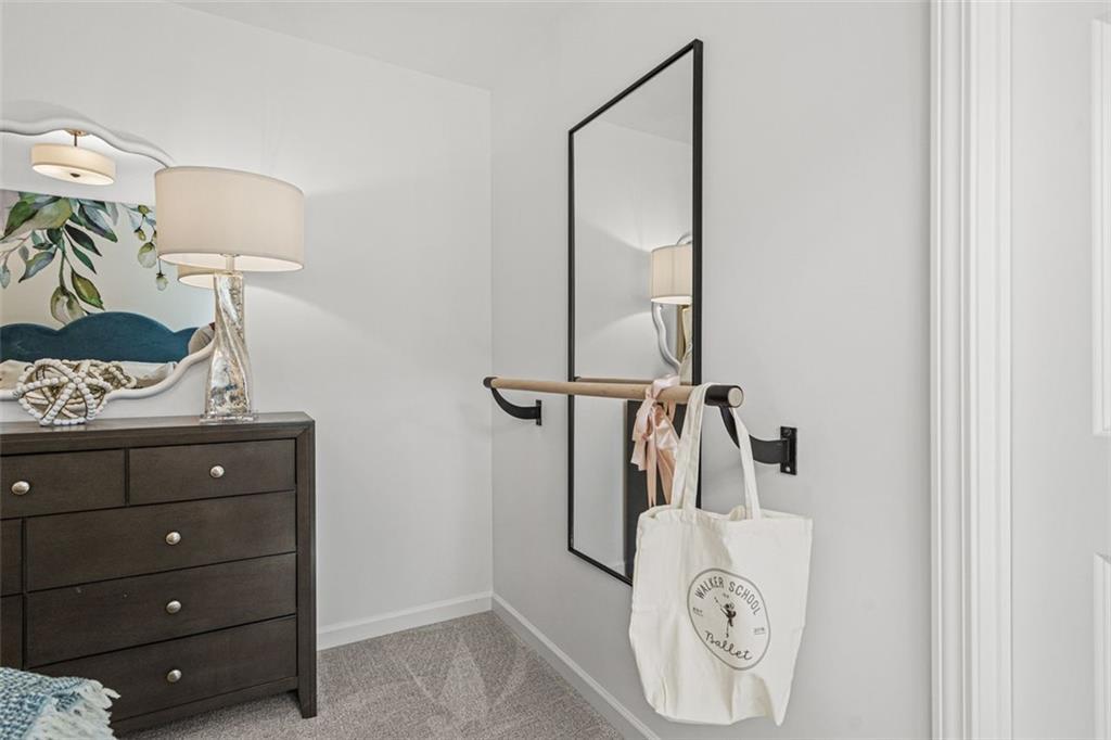 Elegant walk-in closet with large framed mirror, dark wood dresser, decorative lamps, and hanging bar in Davidson Homes The Hickory B, Hoschton, GA