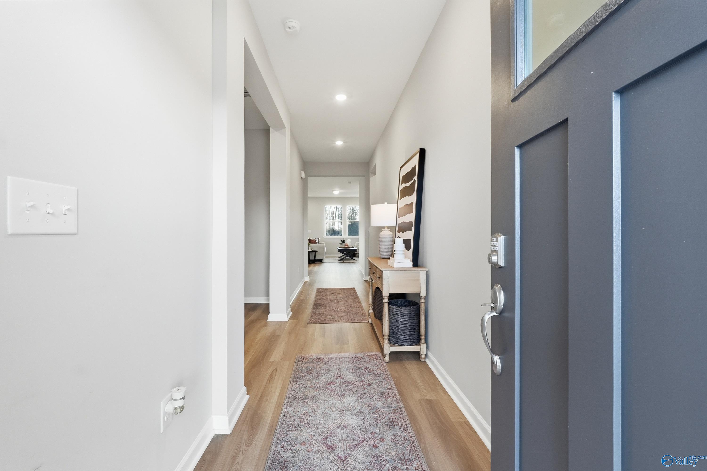 Spacious entry hallway with hardwood floors, runner rug, console table, and open gray front door in Davidson Homes The Polaris, Fayetteville, Tennessee