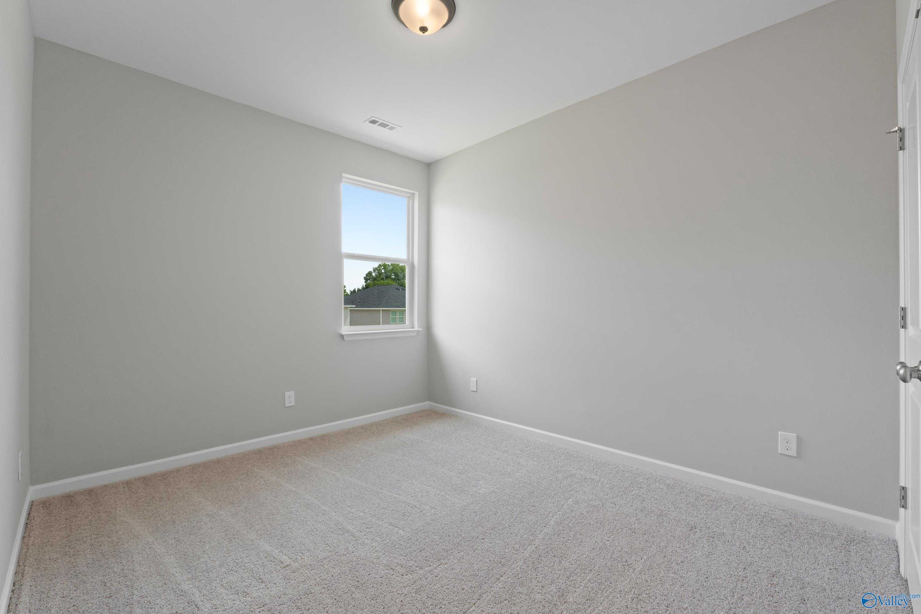 Bright secondary bedroom with neutral gray walls, carpet flooring, and window view in Evermore Homes The Aurora, Harvest AL