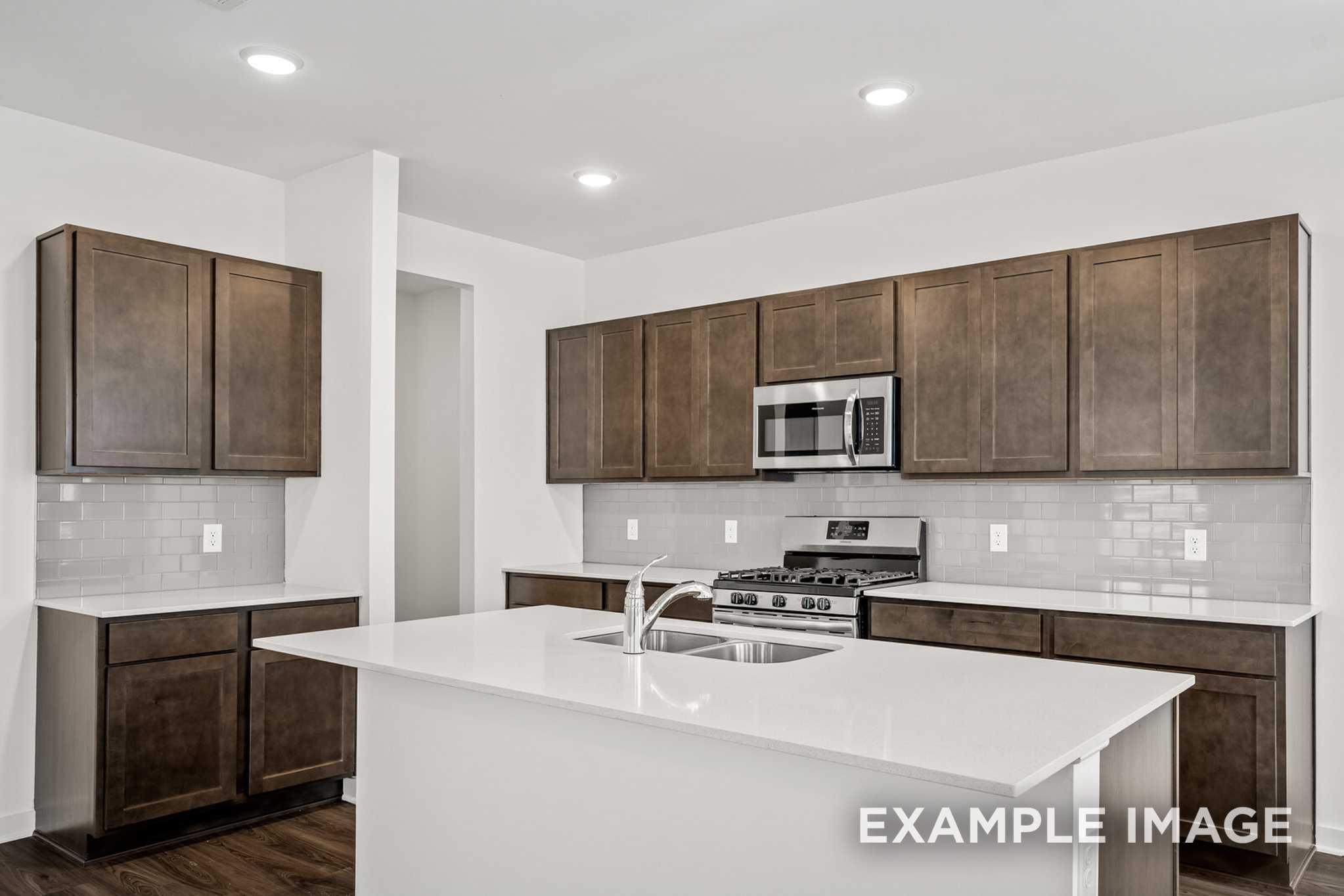 Spacious modern kitchen in The Grayson C by Davidson Homes featuring white quartz island, brown shaker cabinets, stainless appliances, subway tile backsplash