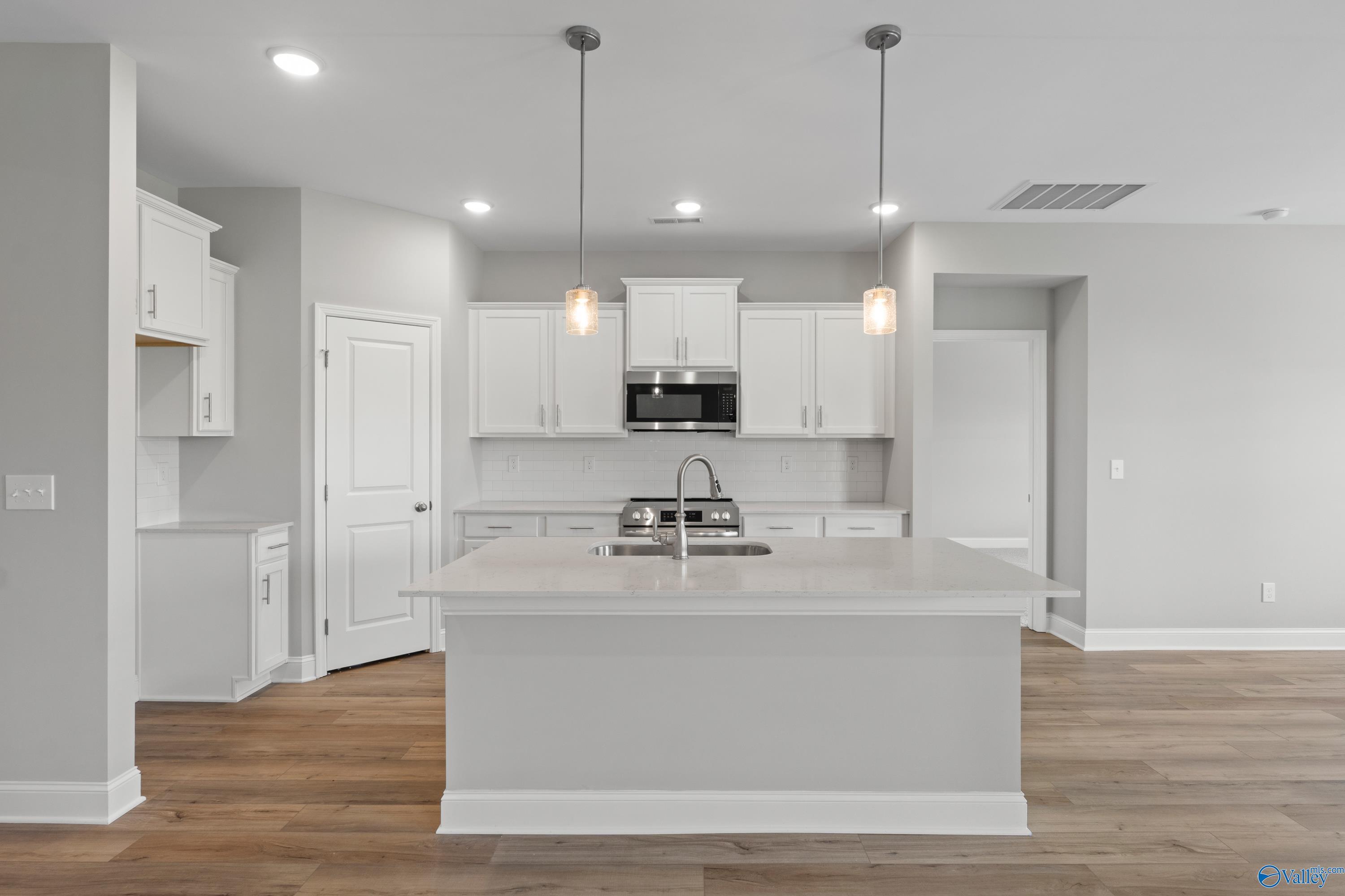 Modern white kitchen with large island sink, stainless steel appliances, and hardwood floors in The Everett B 4-bedroom home, Toney, Alabama