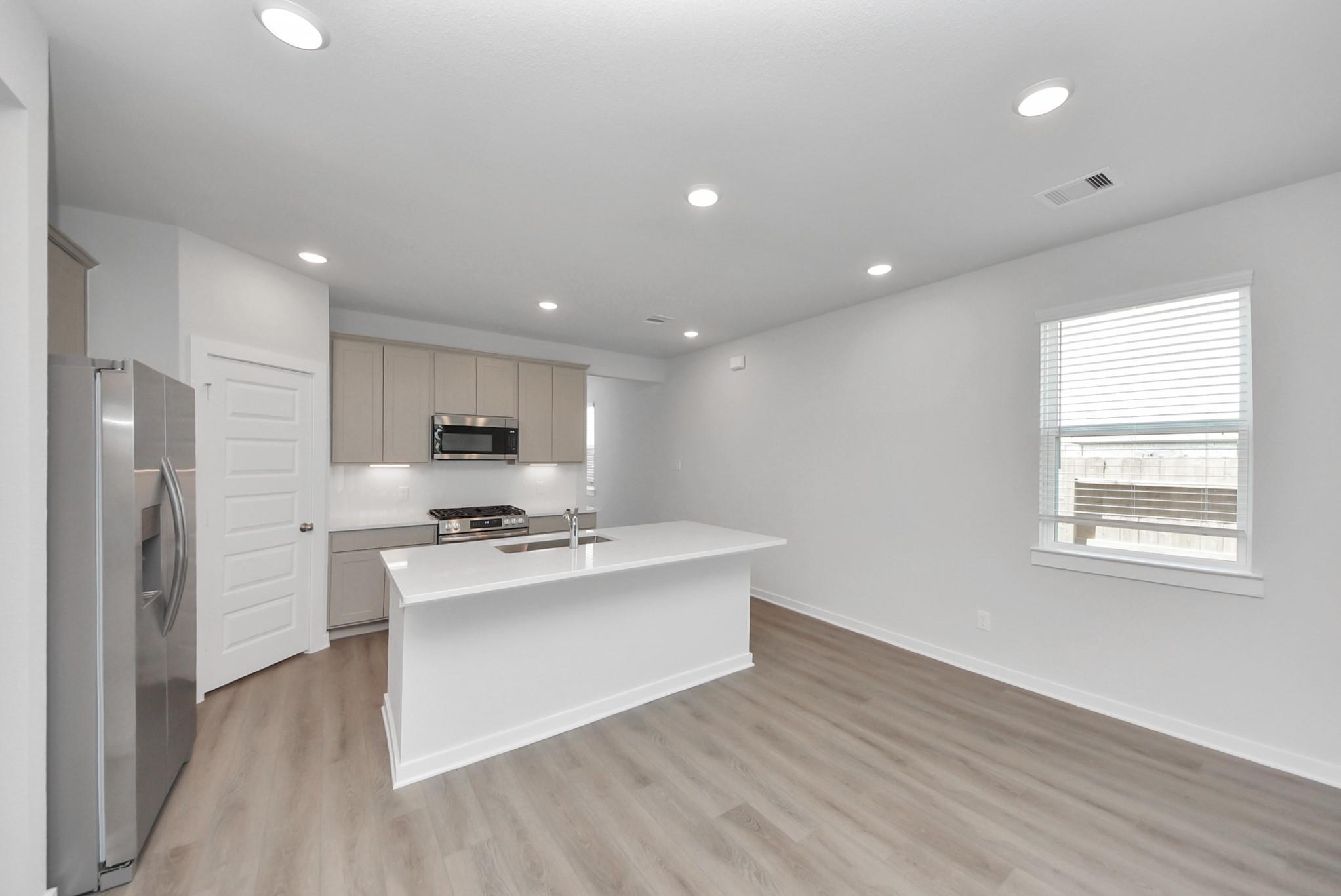 Bright open-concept kitchen with white island, stainless appliances, and wood-look floors in The San Marcos E, Emberly, Beasley TX