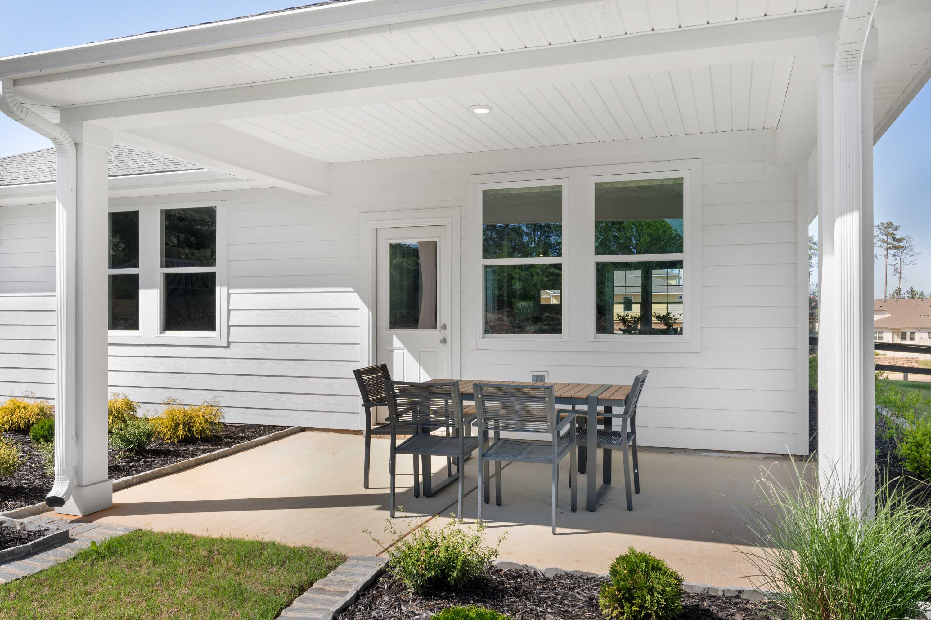 Covered patio with teak dining table and chairs at Evergreen Mill in Madison Alabama, white shiplap exterior and lush landscaping
