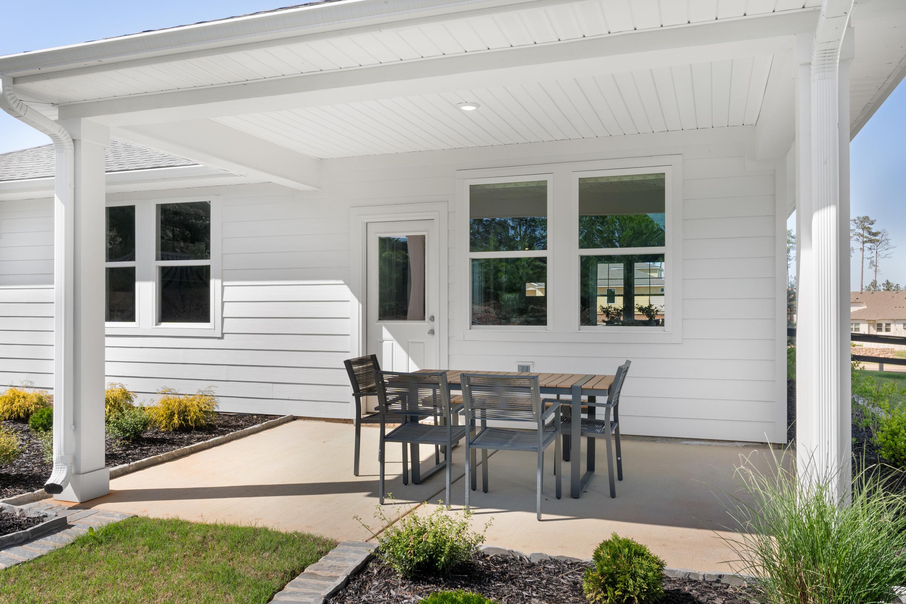 Covered patio with teak dining table and chairs at Evergreen Mill in Madison Alabama, white shiplap exterior and lush landscaping