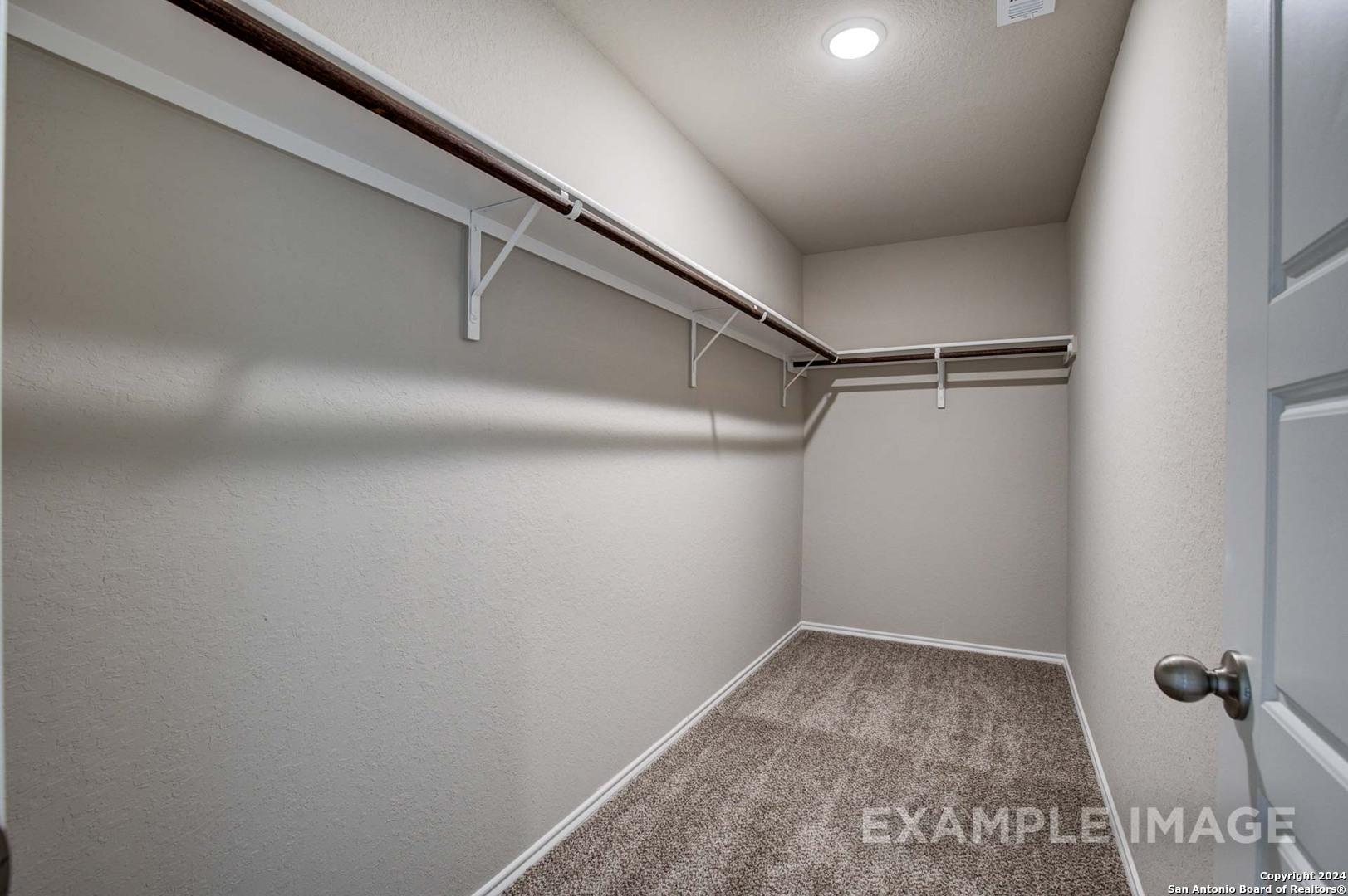Spacious walk-in closet with built-in wooden shelves and carpet floor in Davidson Homes The Murray J, Bricewood, San Antonio