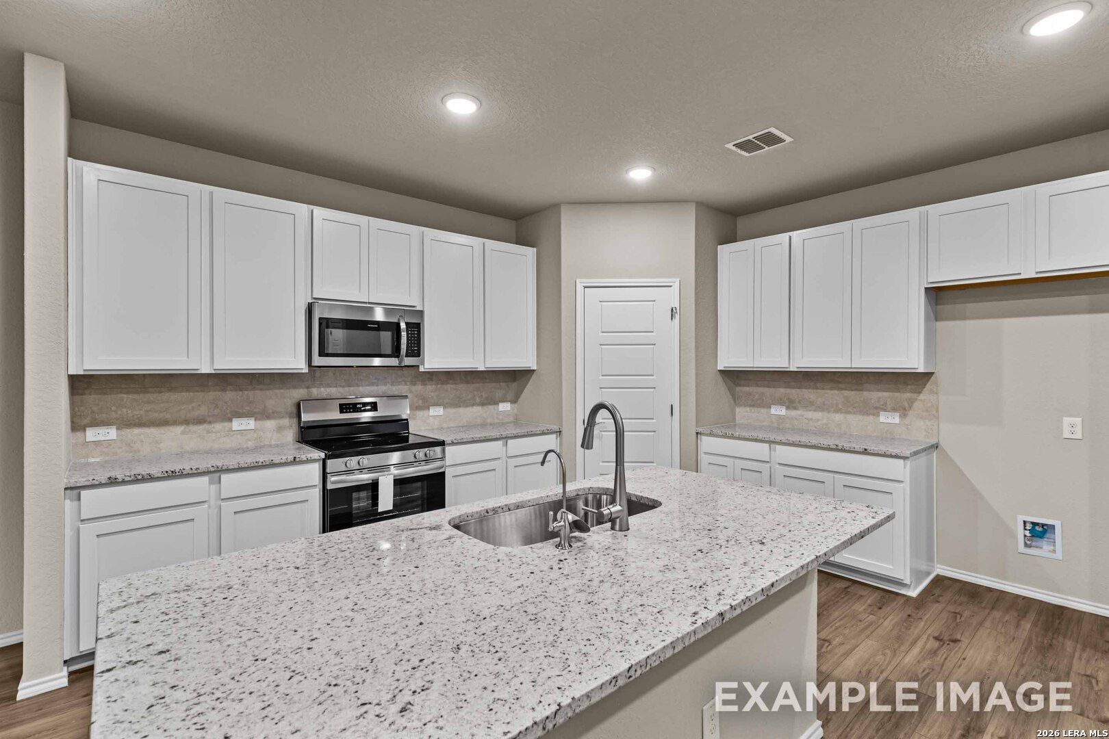 Modern kitchen with white cabinets, granite island, and stainless appliances in The Douglas F floor plan, Bricewood, San Antonio.