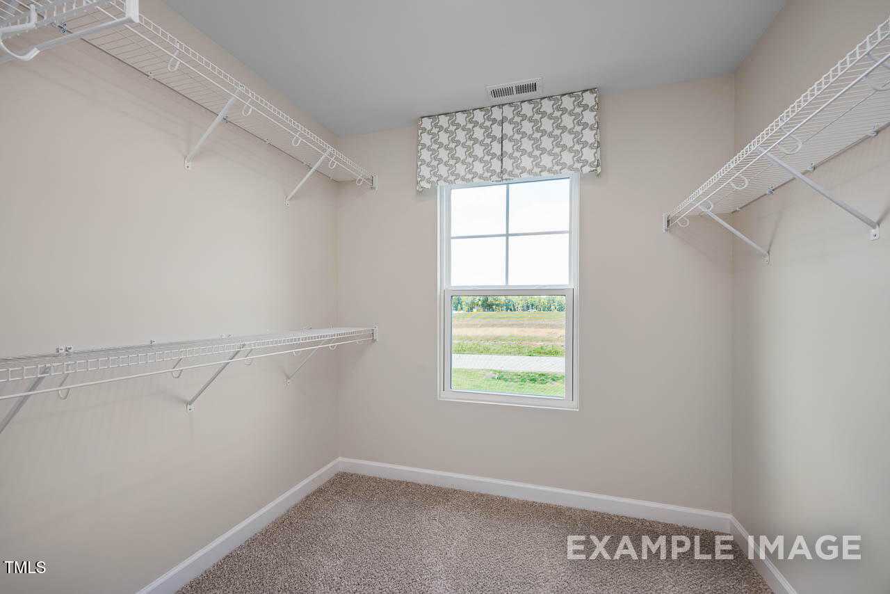 Spacious walk-in closet with wire shelving, beige walls, and window overlooking fields in Davidson Homes The Willow G, Angier, NC