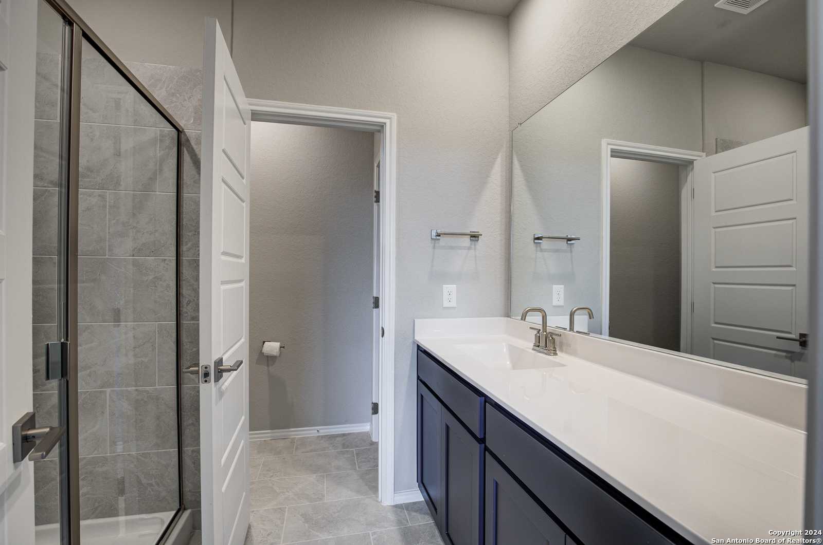 Contemporary master bathroom with frameless glass shower, navy vanity, white quartz countertop, and subway tile in Davidson Homes The Frio B, San Antonio