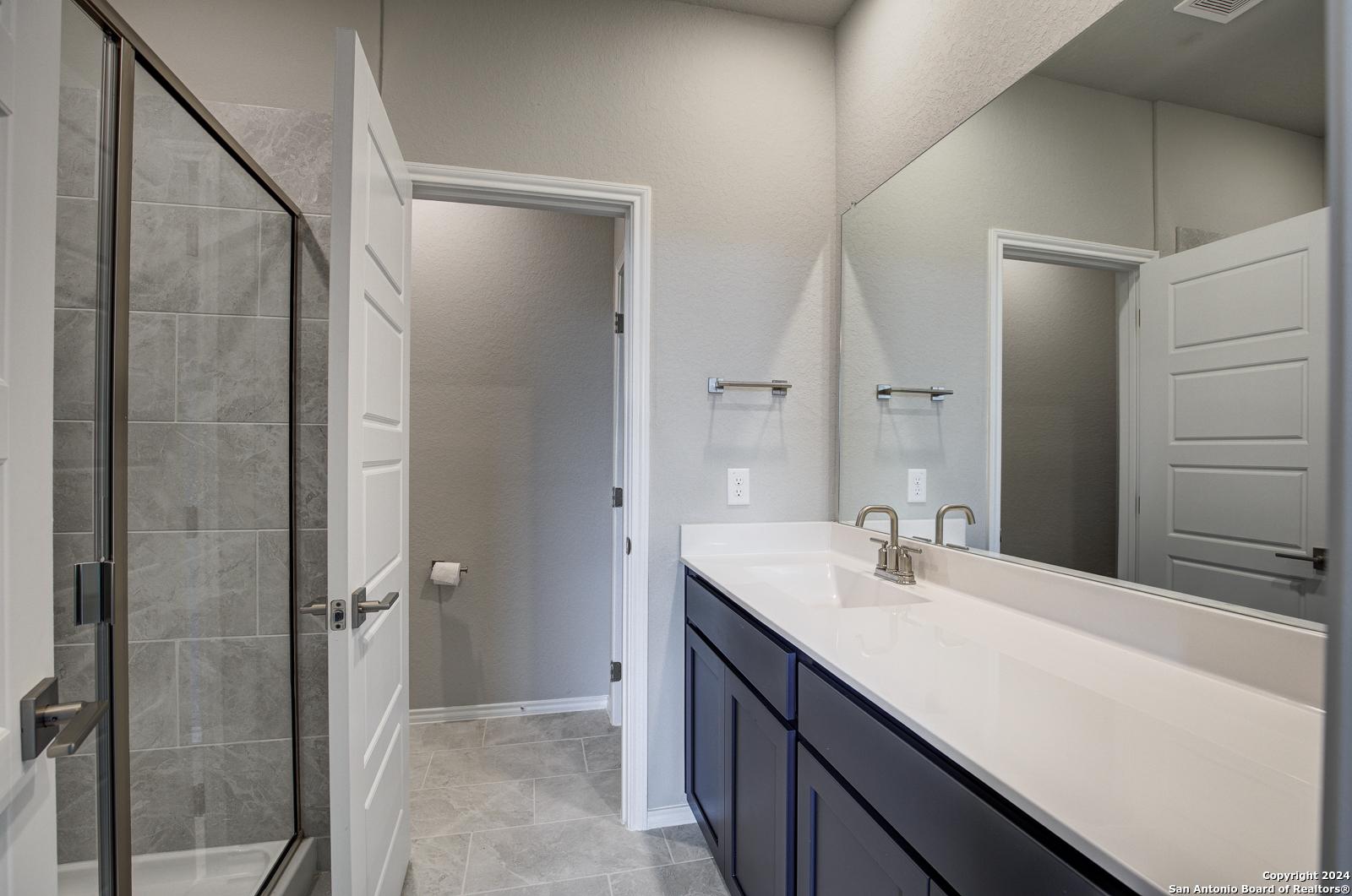 Contemporary master bathroom with frameless glass shower, navy vanity, white quartz countertop, and subway tile in Davidson Homes The Frio B, San Antonio