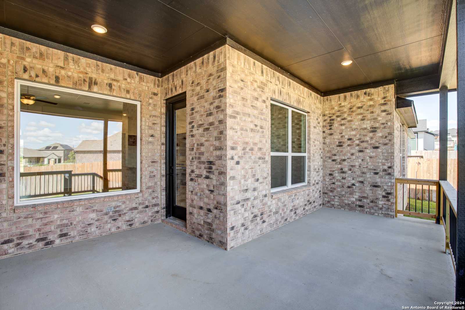 Covered brick patio with dark ceiling, large screened windows, and French door in Davidson Homes The Garner B, Castroville, Texas
