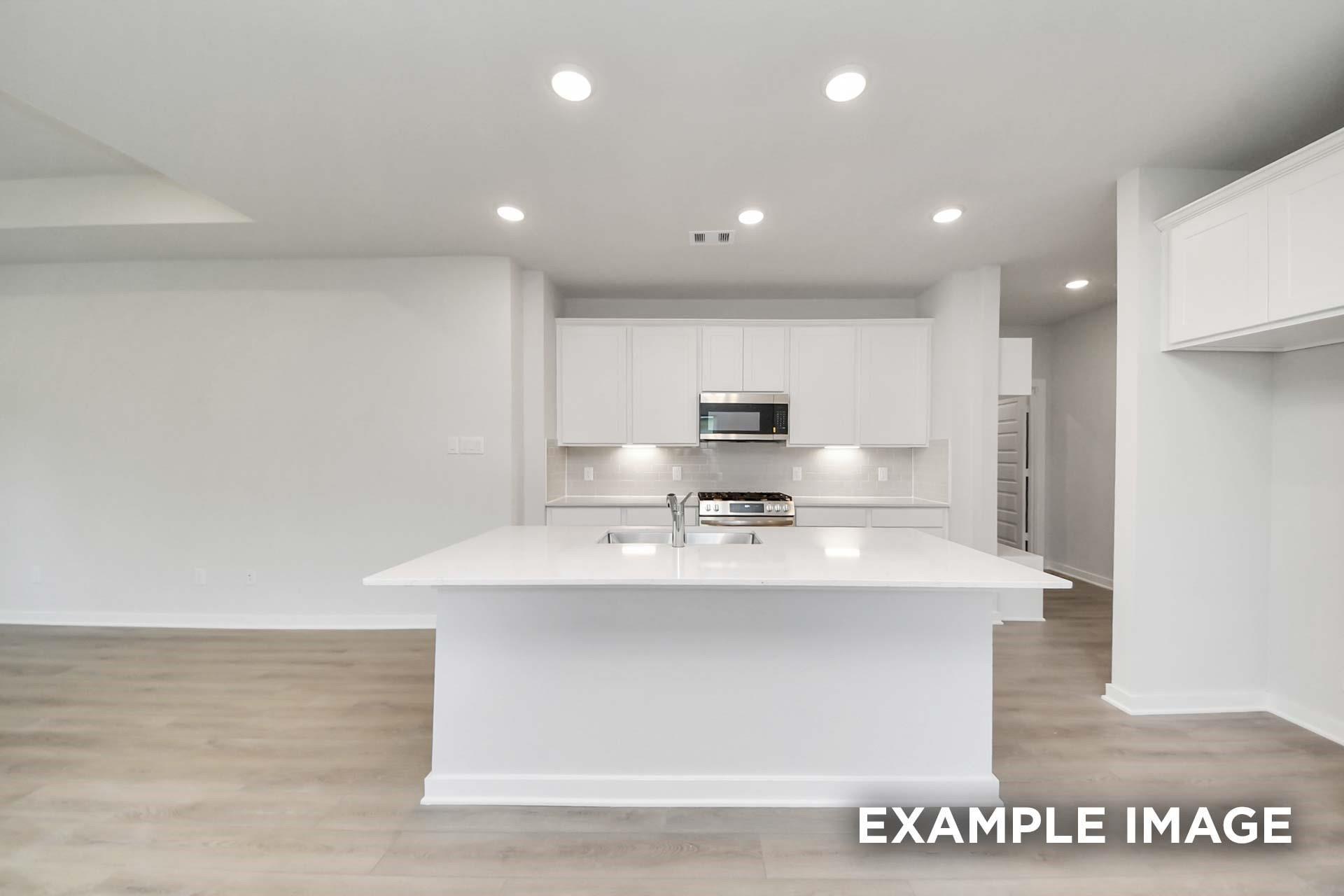 Bright white kitchen with large island, sink, stainless gas range, and microwave in Davidson Homes The Blanco E, Magnolia, Texas