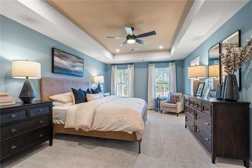Serene master bedroom with soft blue walls, tray ceiling fan, king bed, and large windows in Davidson Homes The Marion C, Winder, Georgia