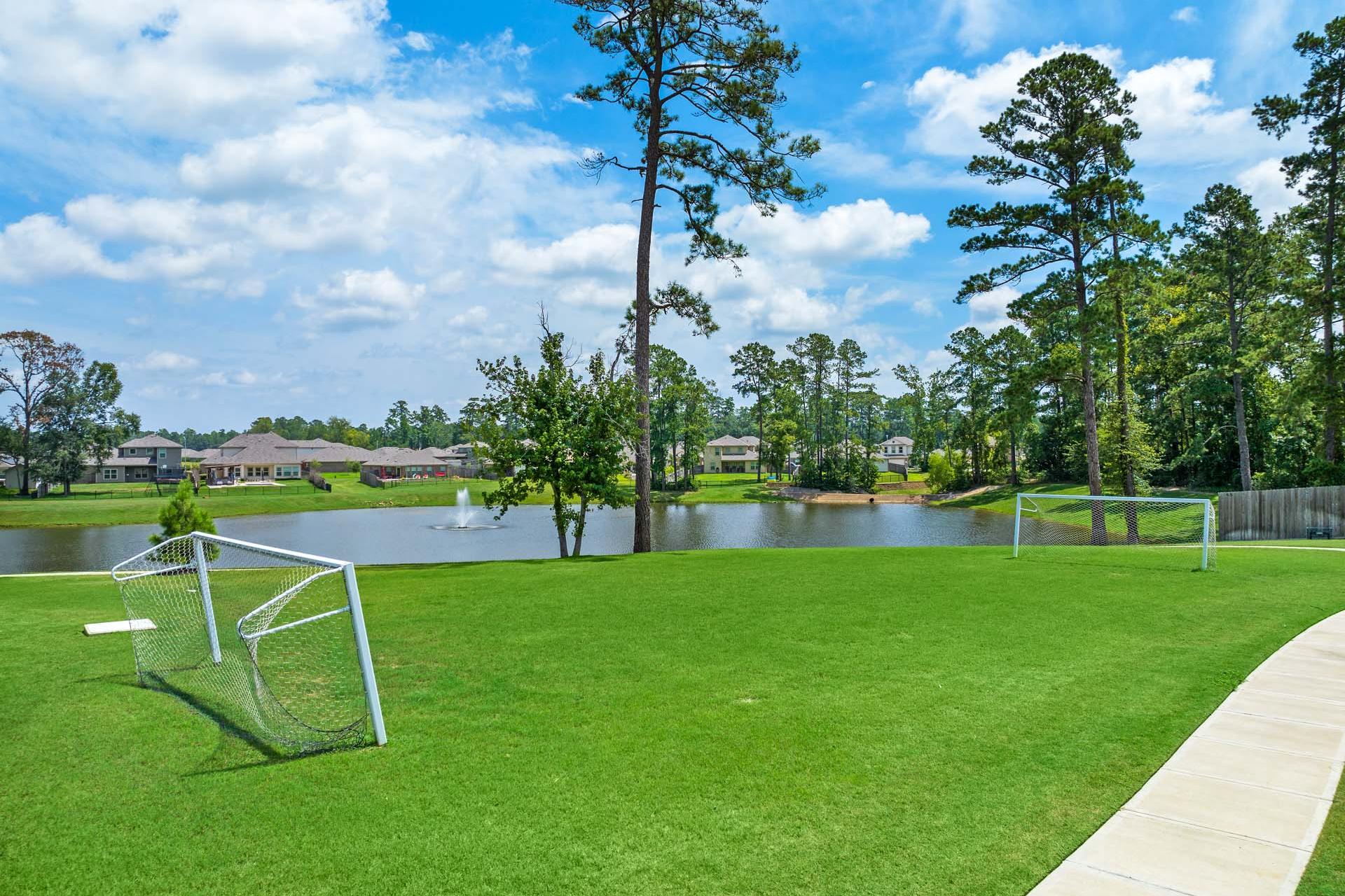 Soccer goals on lush green field by scenic lake at Lakes at Black Oak in Magnolia, Texas with pine trees and homes