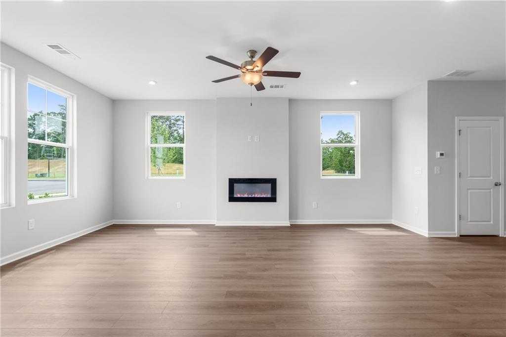 Bright living room with modern gas fireplace, ceiling fan, hardwood floors, and large windows in Davidson Homes The Monroe A, Emerson, GA