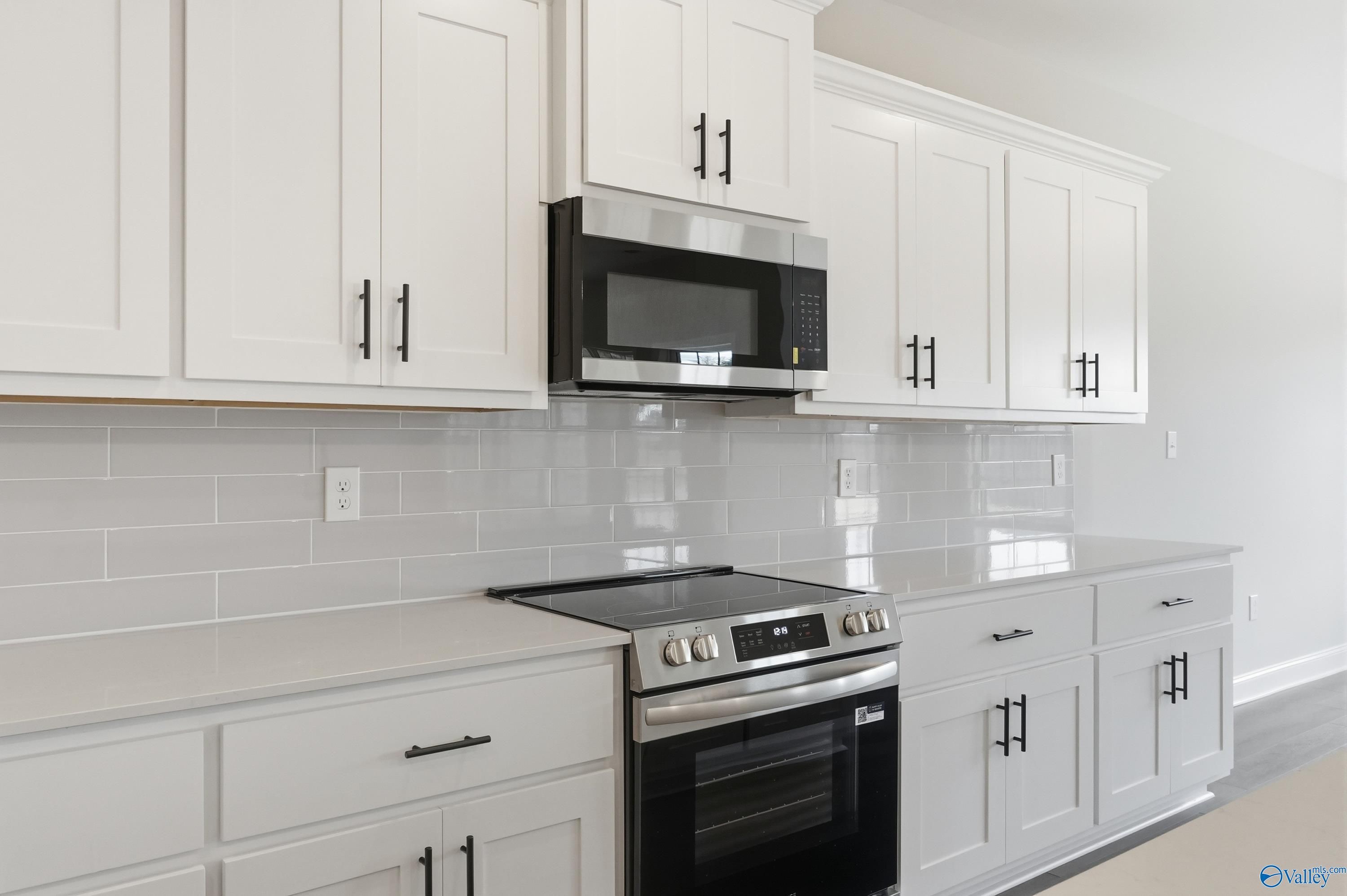 Modern white kitchen with shaker cabinets, stainless microwave, oven, subway tile backsplash in Davidson Homes The Finleigh, Meridianville, AL