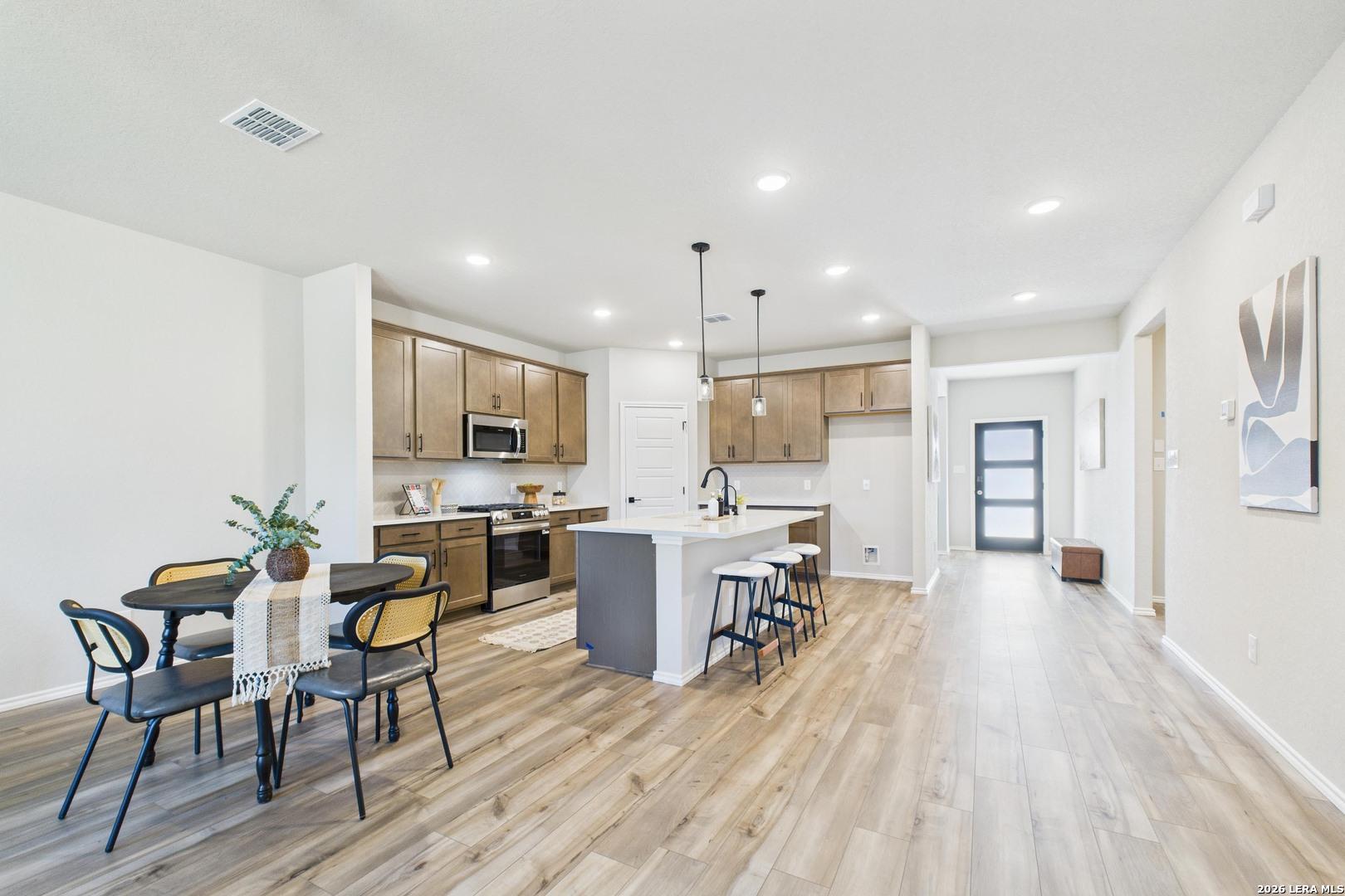 Modern kitchen featuring light wood cabinets, white quartz island with bar stools, stainless appliances, and open dining area in Davidson Homes The Douglas E, Bricewood, San Antonio