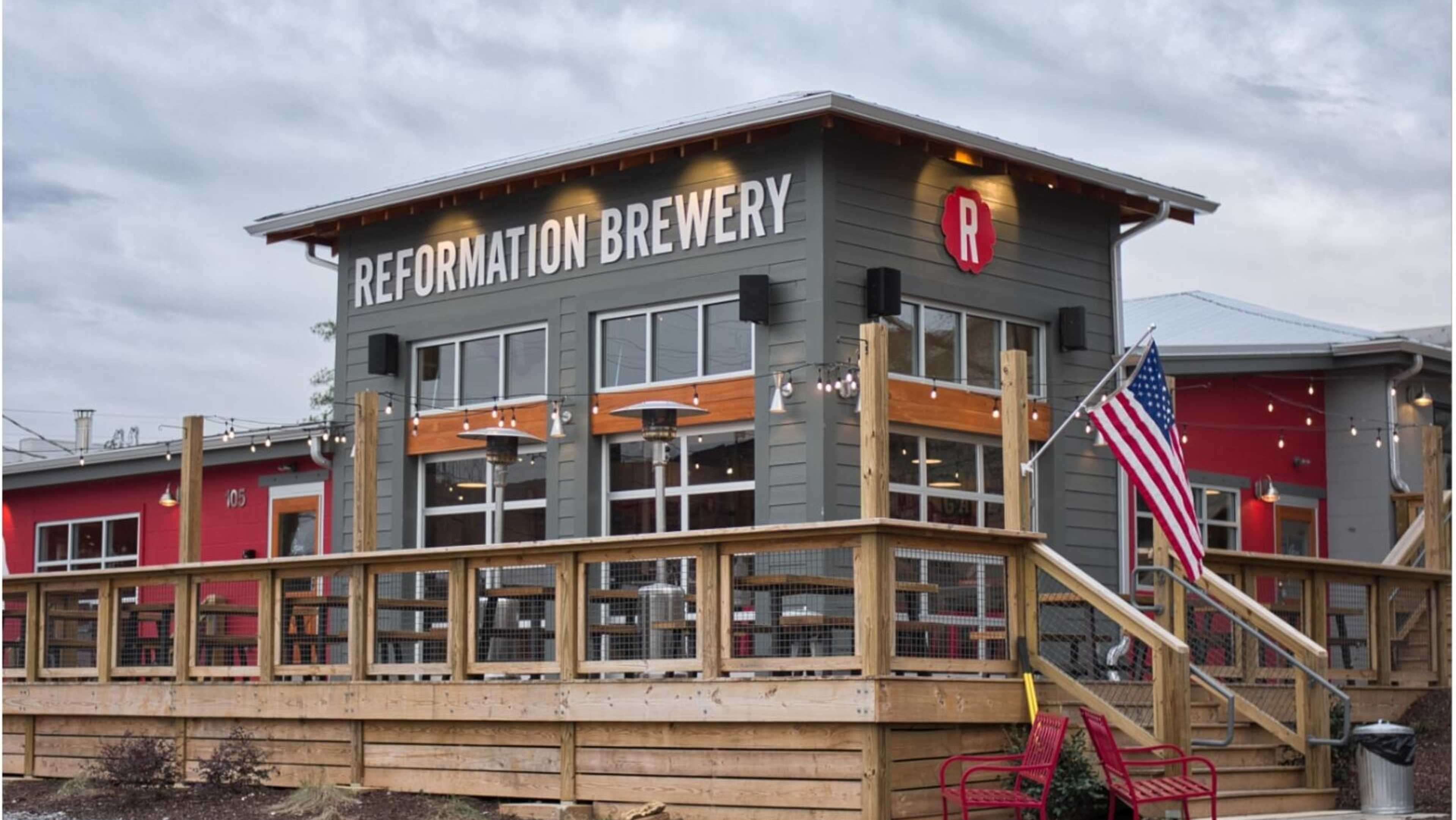 Reformation Brewery in Woodstock GA: rustic exterior with signage, wooden deck, red chairs, and American flags