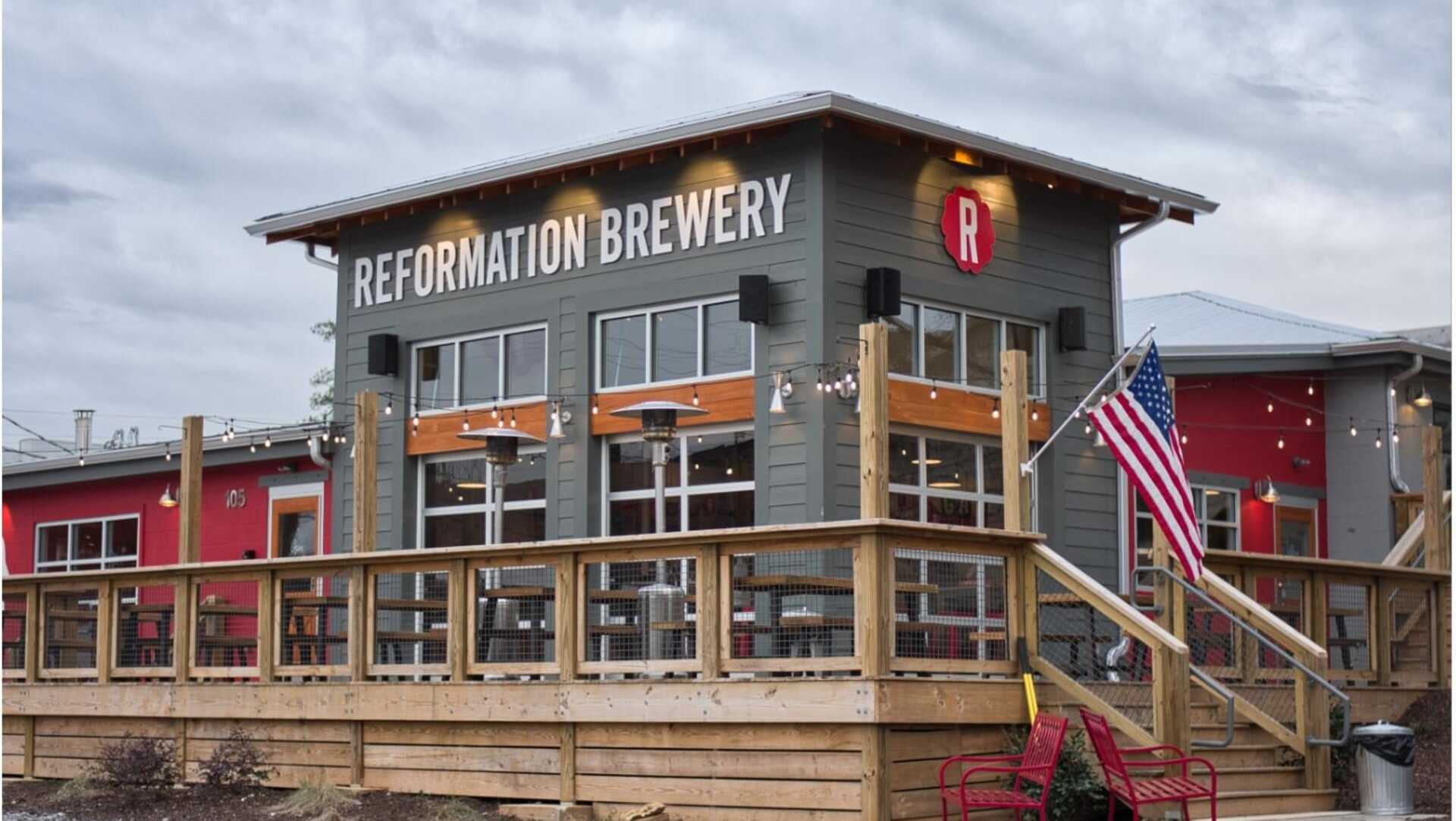 Reformation Brewery in Woodstock GA: rustic exterior with signage, wooden deck, red chairs, and American flags