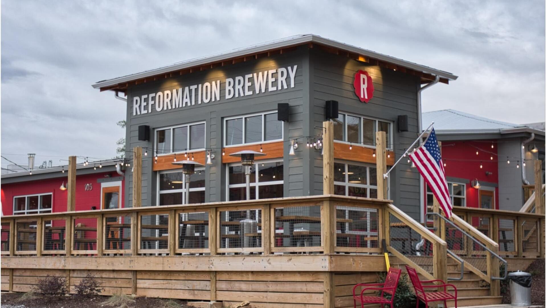 Reformation Brewery in Woodstock GA: rustic exterior with signage, wooden deck, red chairs, and American flags