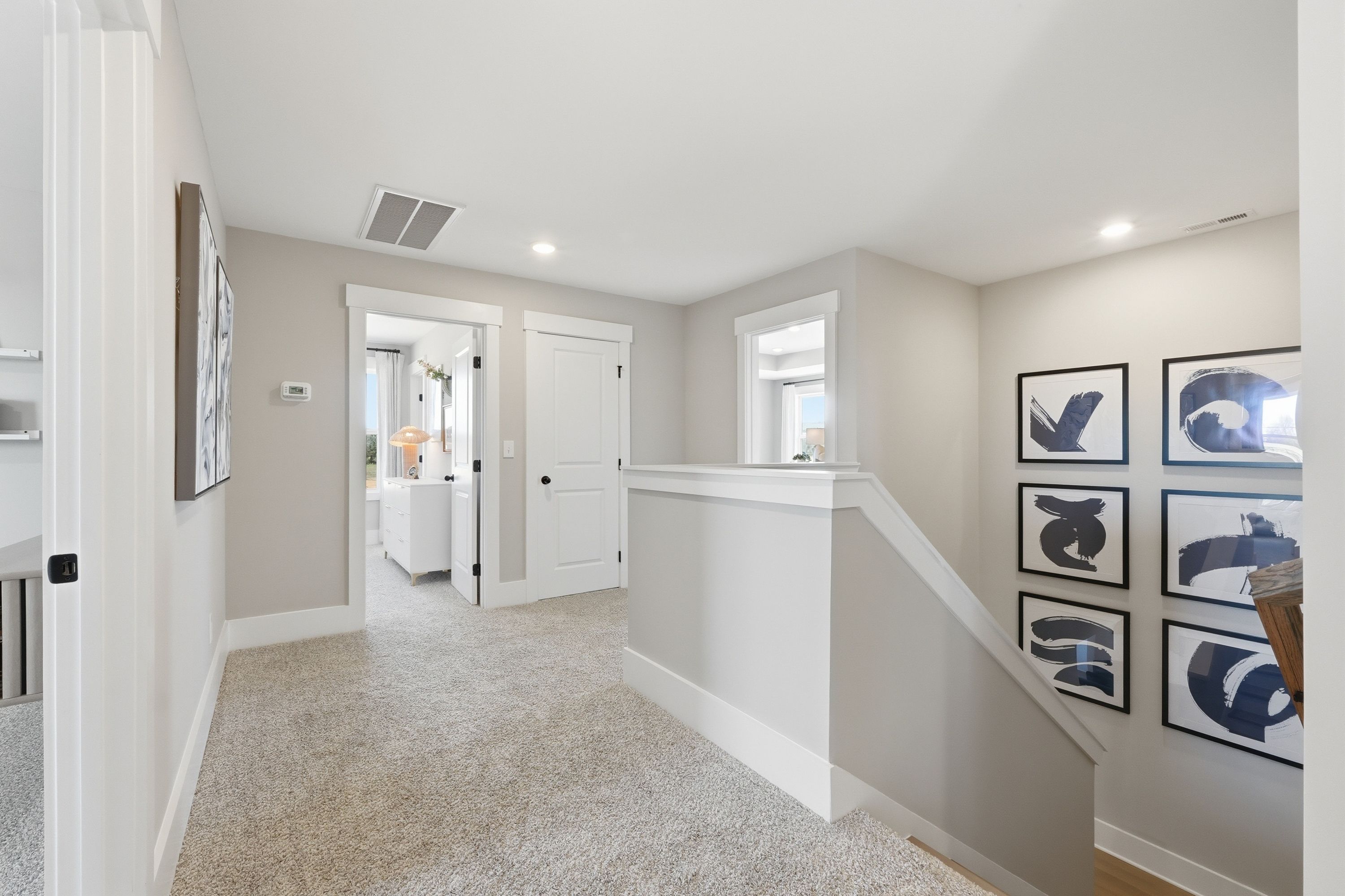 Spacious upstairs hallway in Berry Cove, New Market AL with beige carpet, white staircase, and abstract black art