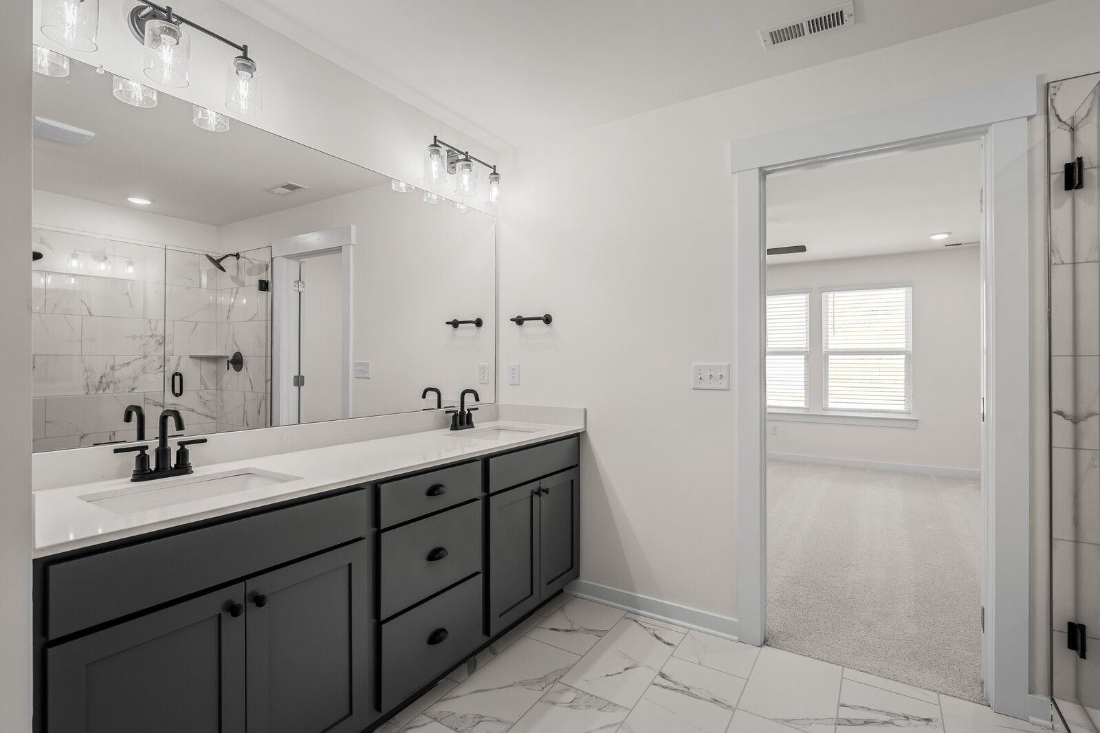 Modern bathroom with double vanity, dark cabinets, and marble-look tile in The Willow floor plan at Woods Crossing, Gallatin.