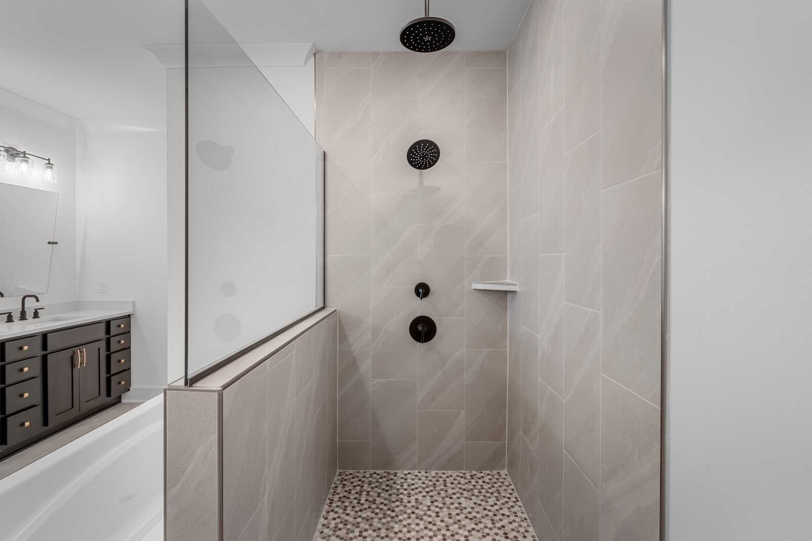 Modern master bathroom with frameless glass shower, rain showerhead, pebble floor tile, and freestanding tub in Davidson Homes The Hathaway, Murfreesboro, TN