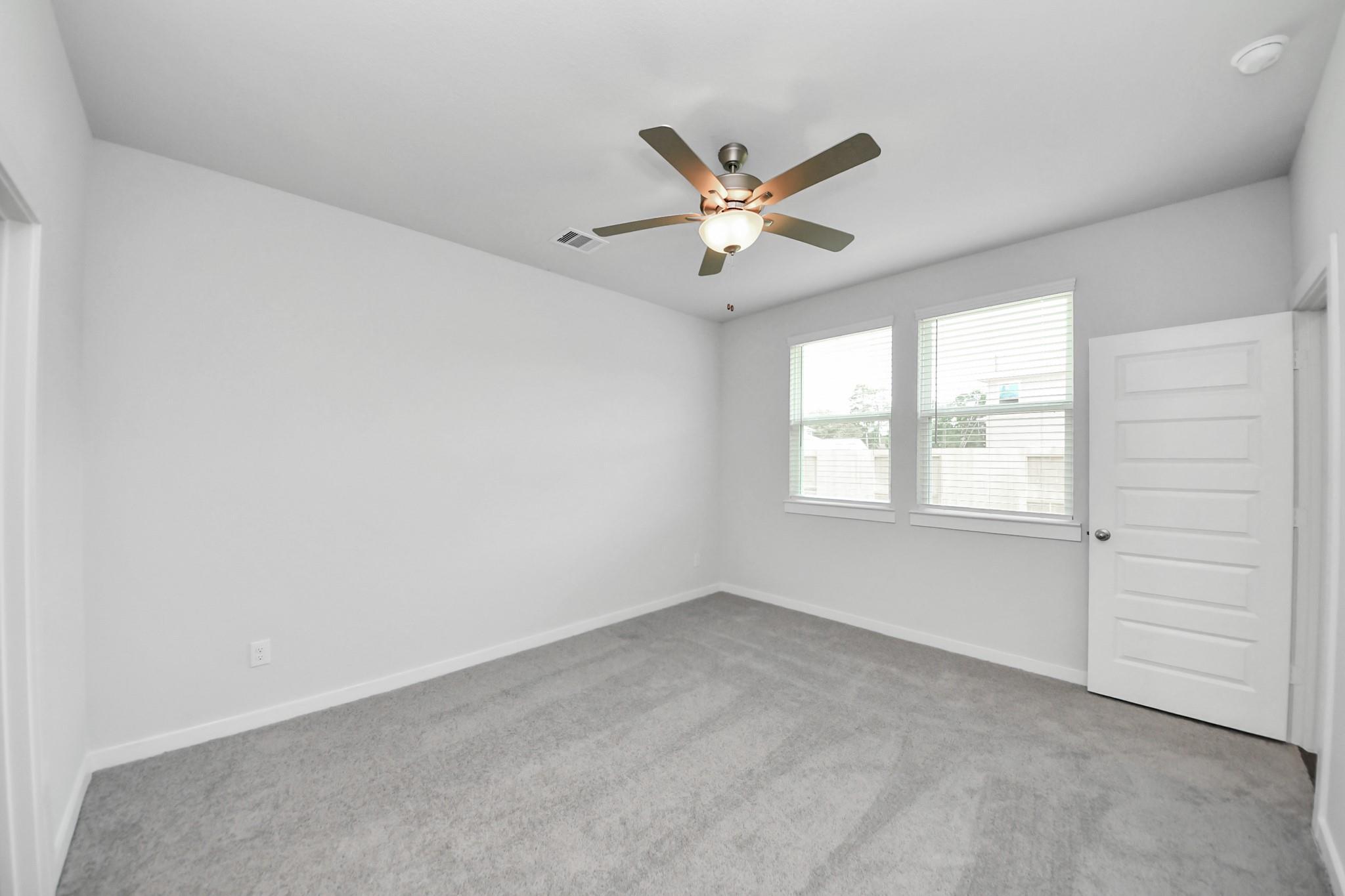 Bright, carpeted bedroom with ceiling fan and large windows in The Brazos F floor plan at Liberty Estates, Cleveland, TX.