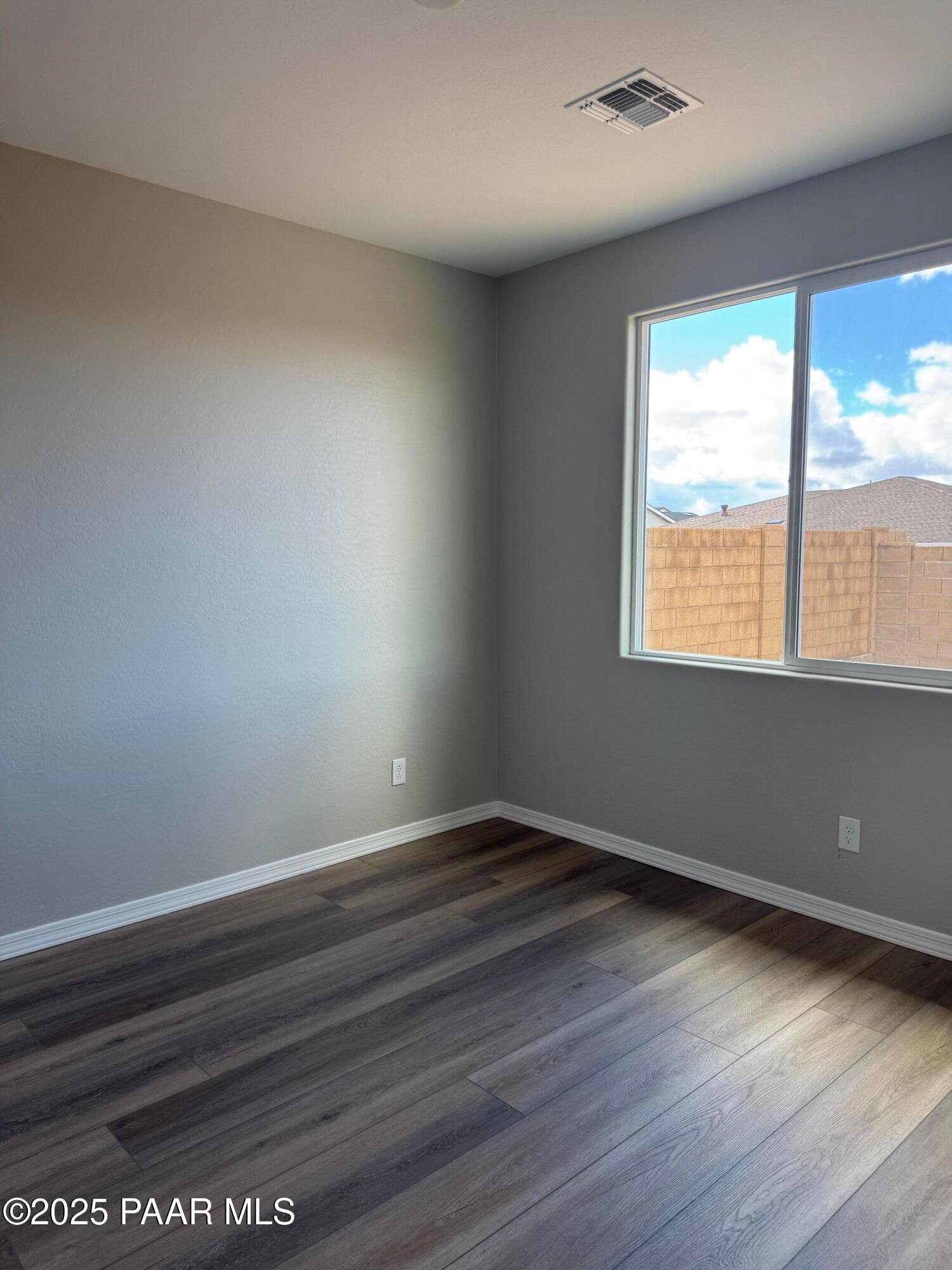 Bright empty room with gray walls, luxury vinyl plank wood flooring, and large window overlooking Prescott, AZ neighborhood in The Monarch A home